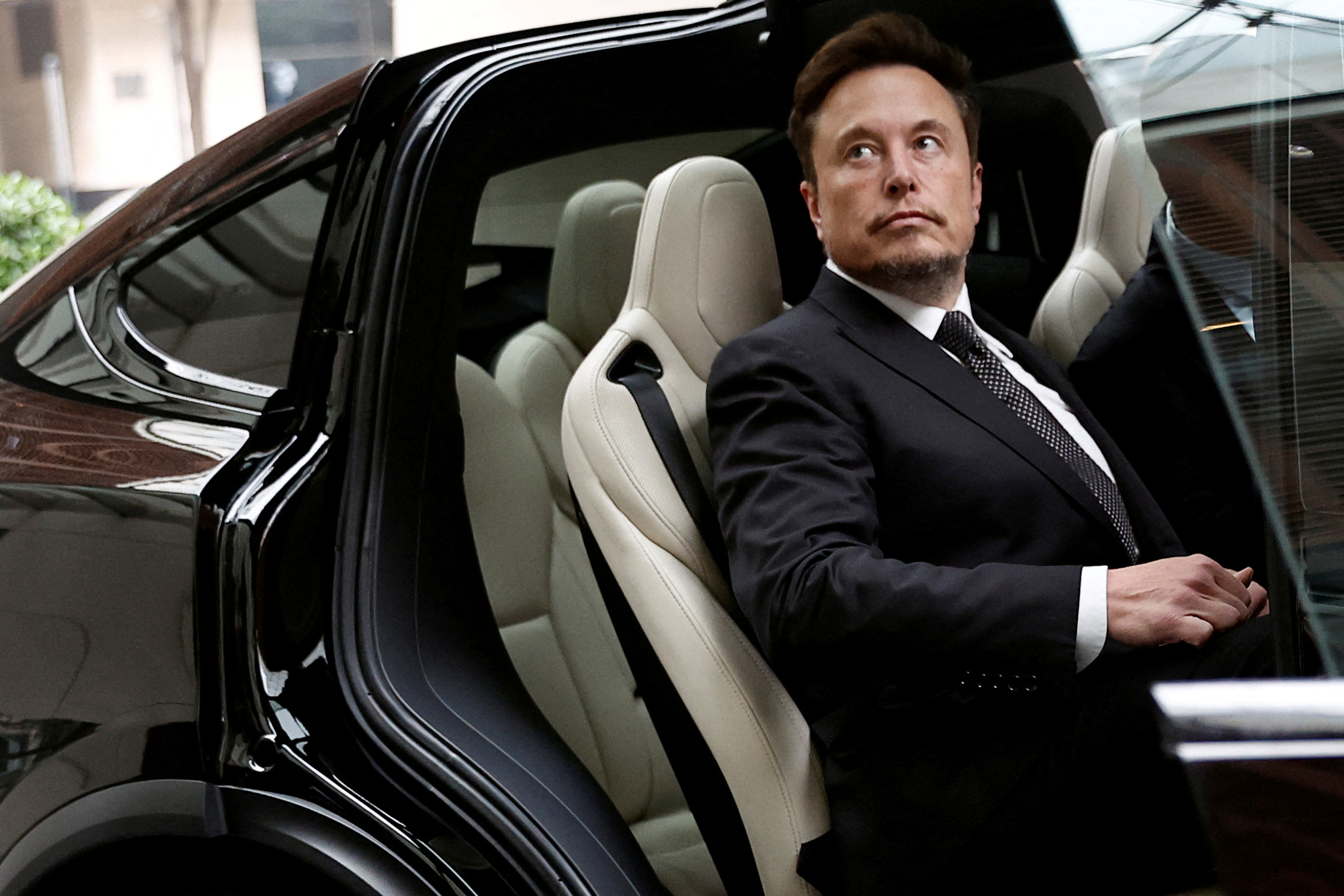 Elon Musk sits in a Tesla with the door open.