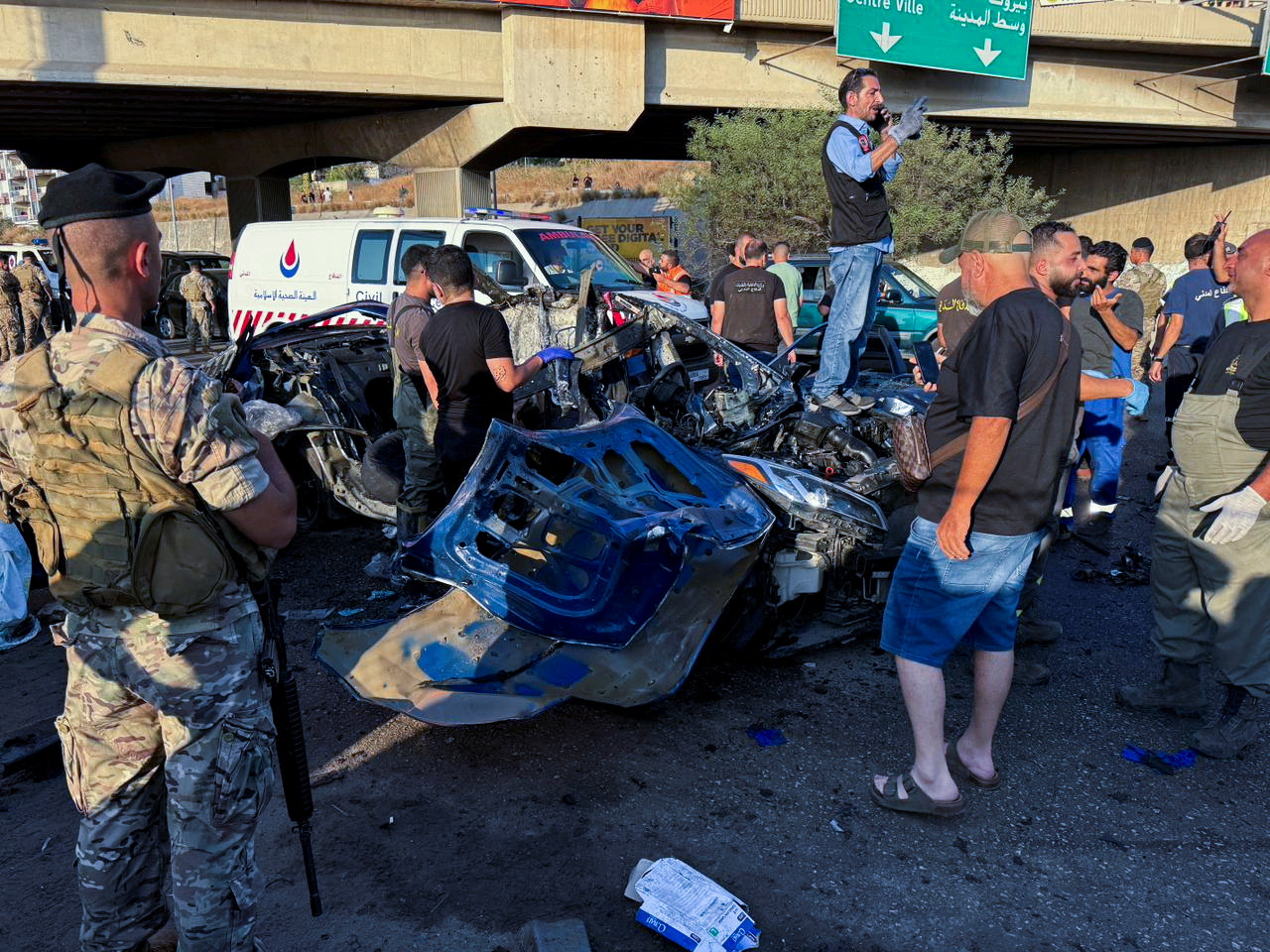 Members of the Lebanese army and people gather near a damaged car.