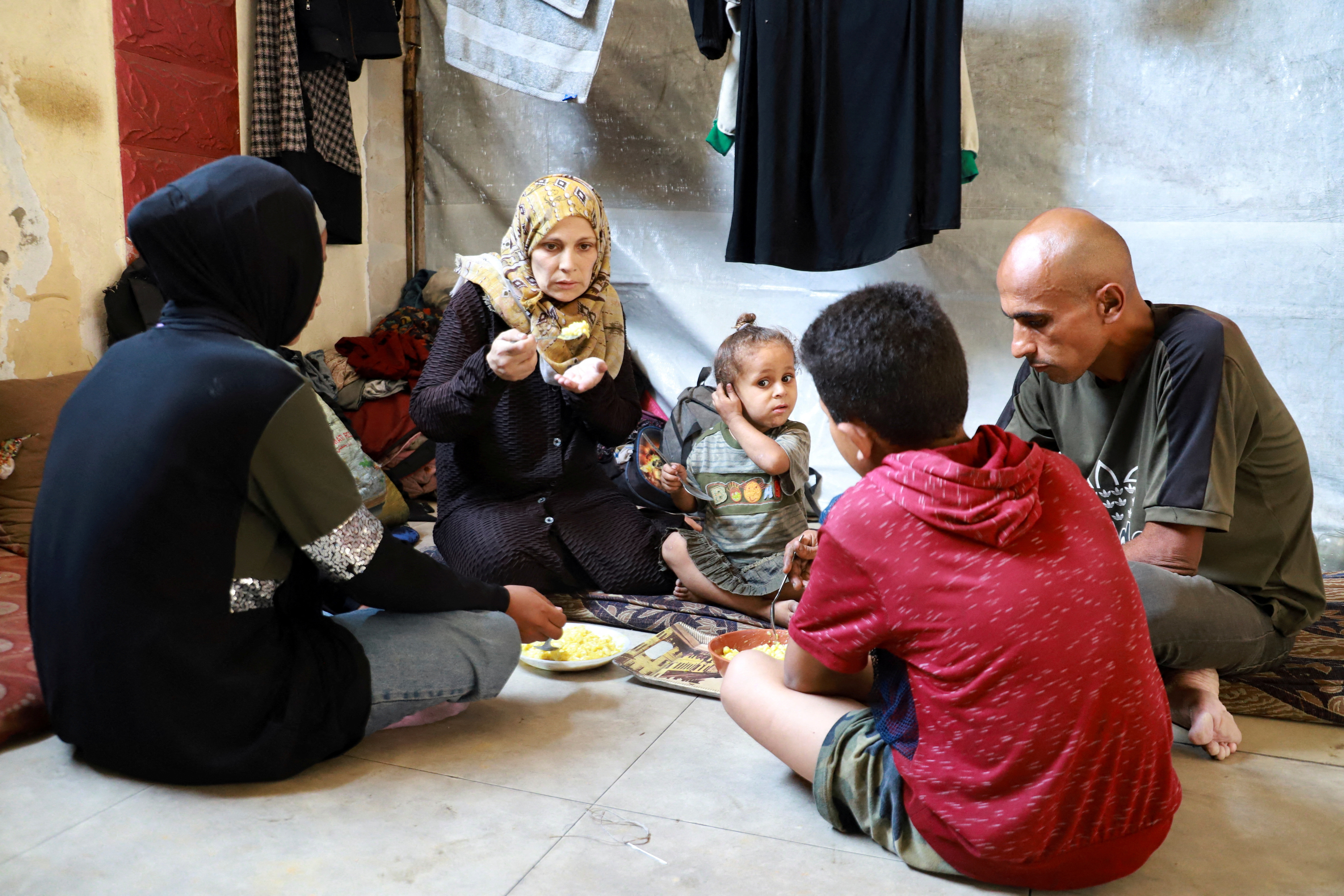 A displaced family eats a meal inside a tent.