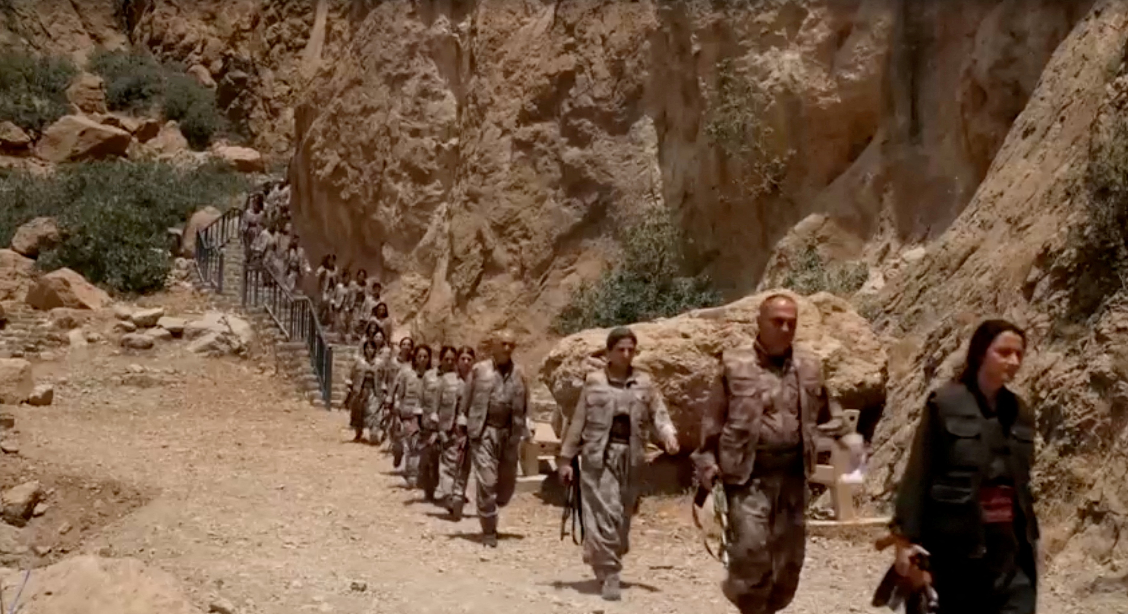 Armed PKK fighters walk on a mountain path.