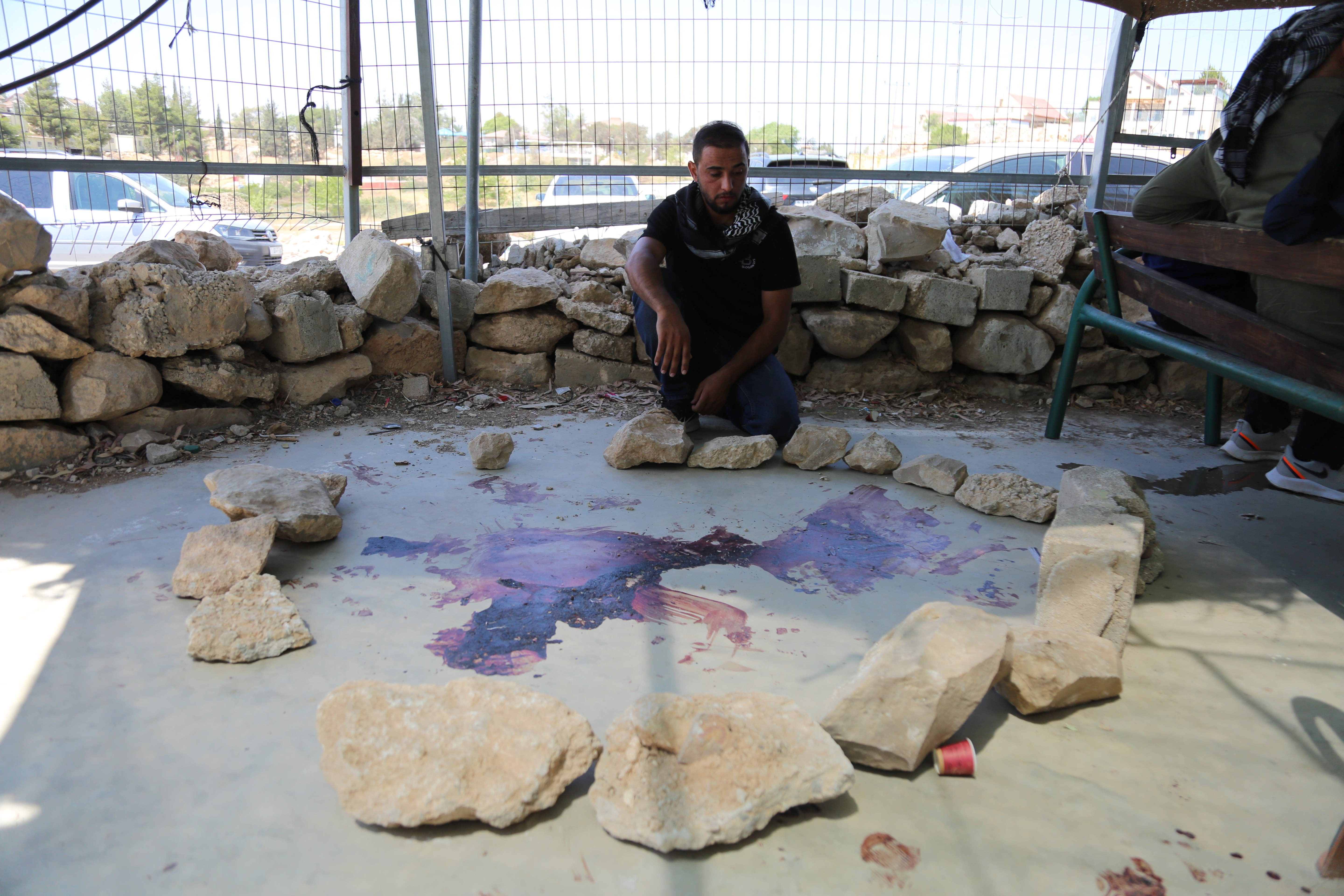 Alaa crouches next to a big bloodstain on the ground, which the villagers have encircled with rocks as a memorial of sorts to the slain Awdah