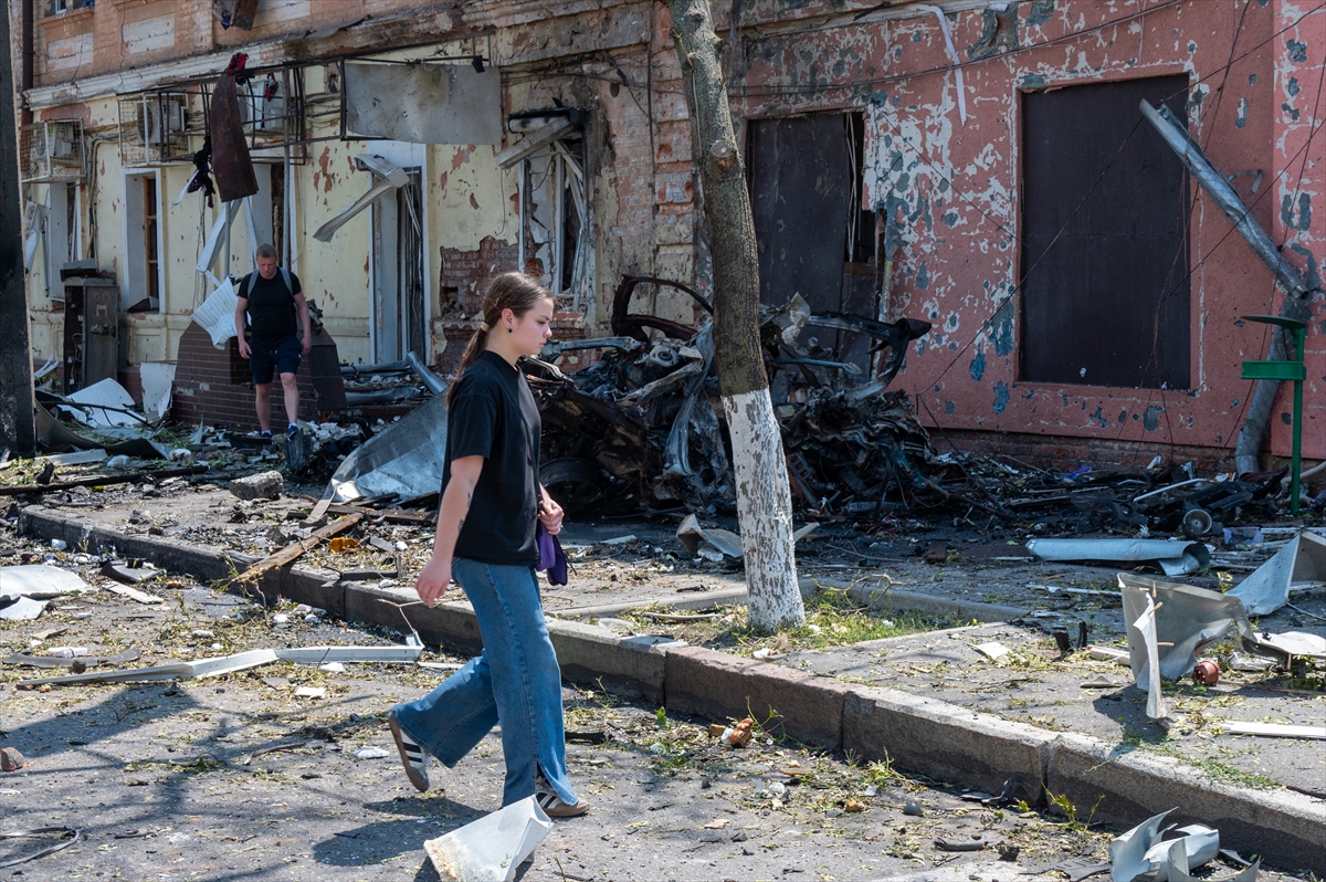 a woman walks past a burnt out car in a street