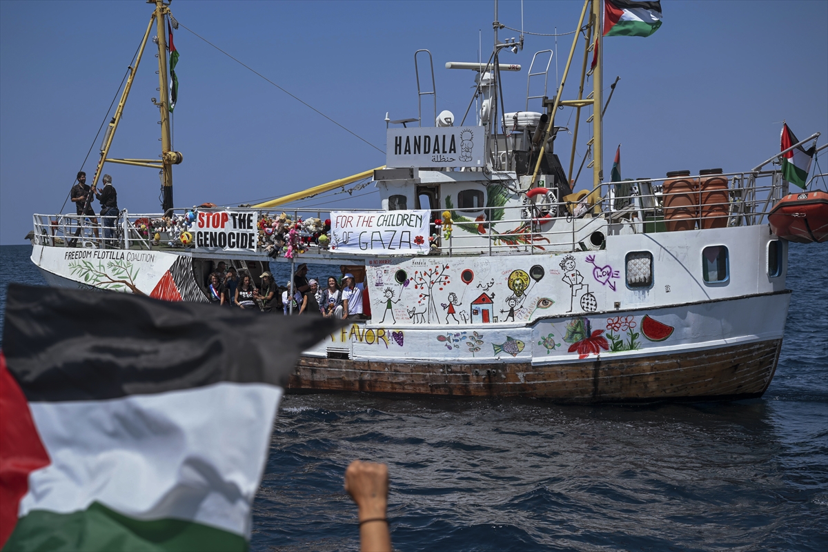 people on a white ship with a sign saying handala and palestinian flags