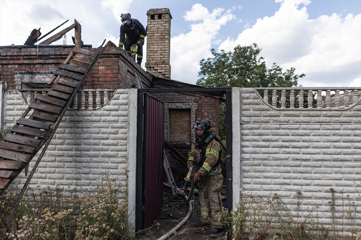firefighters stand on the roof of a rural building as another firefighter stands nearby