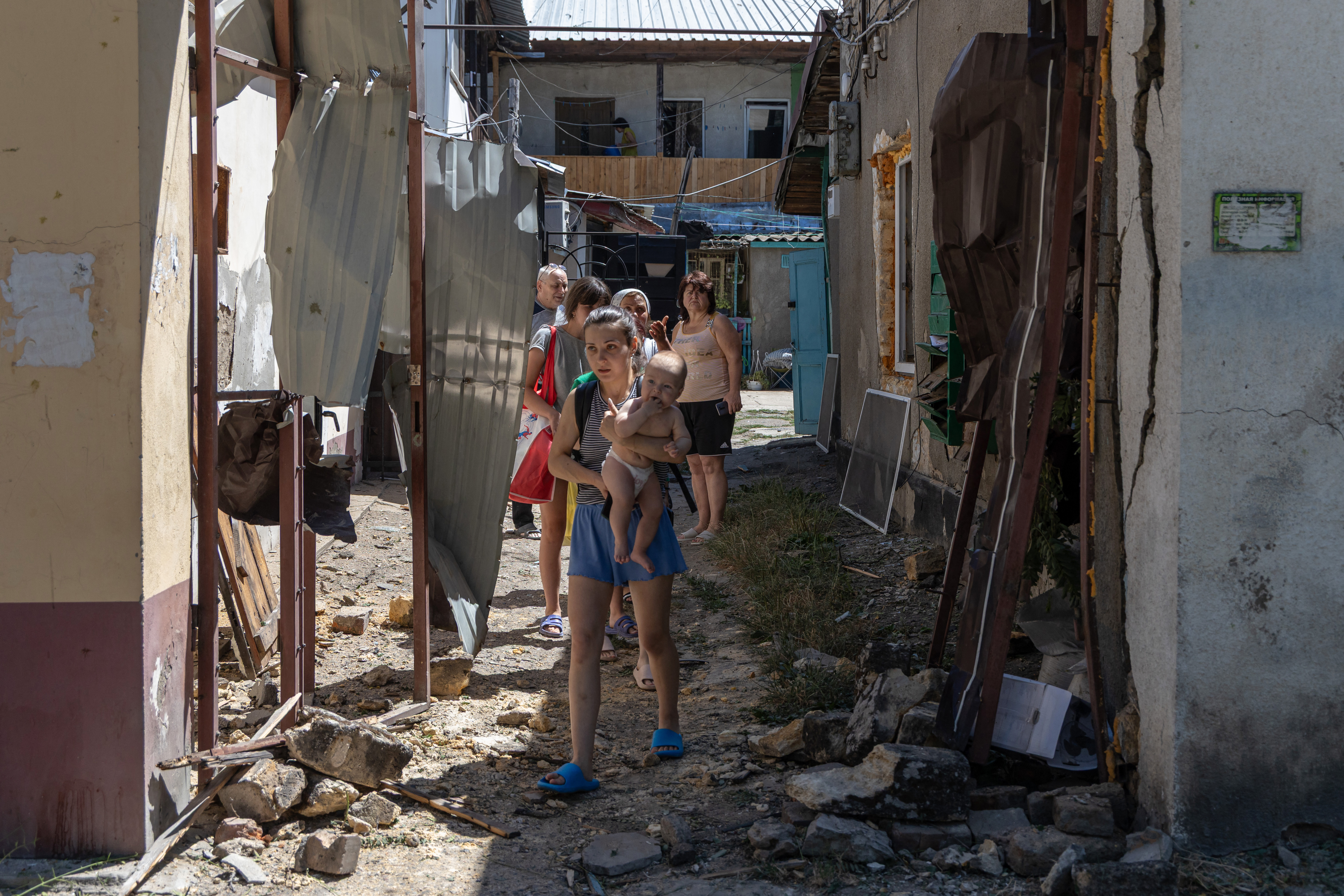 TOPSHOT - A young woman and local resident carries her baby outside residential houses following Russian drone strikes in Odesa, on July 11, 2025, amid the Russian invasion of Ukraine. The southern Ukrainian port city of Odesa was struck later in the morning of July 11, 2025, wounding eight people, local officials said. (Photo by Oleksandr GIMANOV and Oleksandr GIMANOV / AFP)