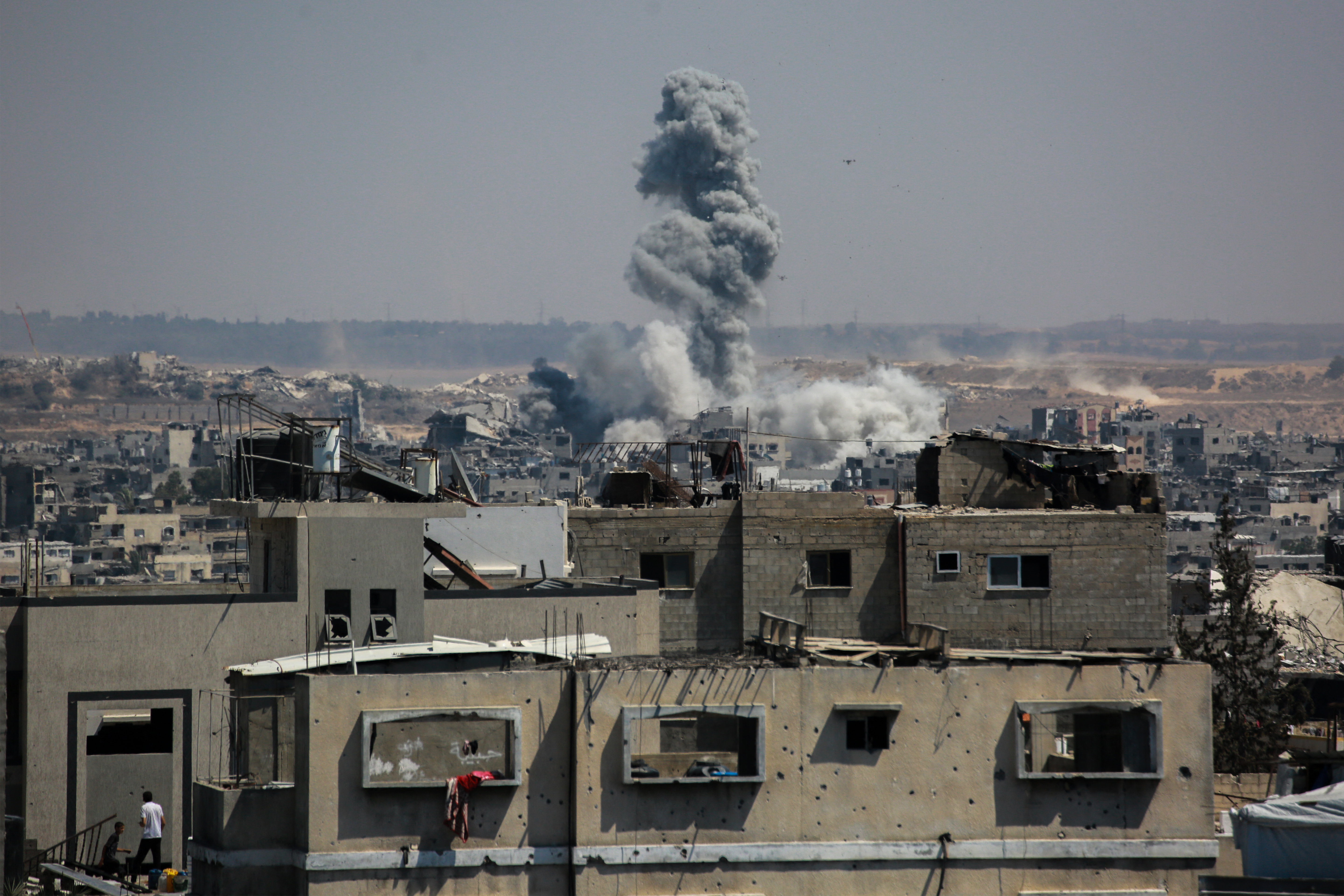 Two Palestinians stand on the roof of a building as smoke billows following Israeli strikes on Jabalia, in the northern Gaza Strip on July 13, 2025.