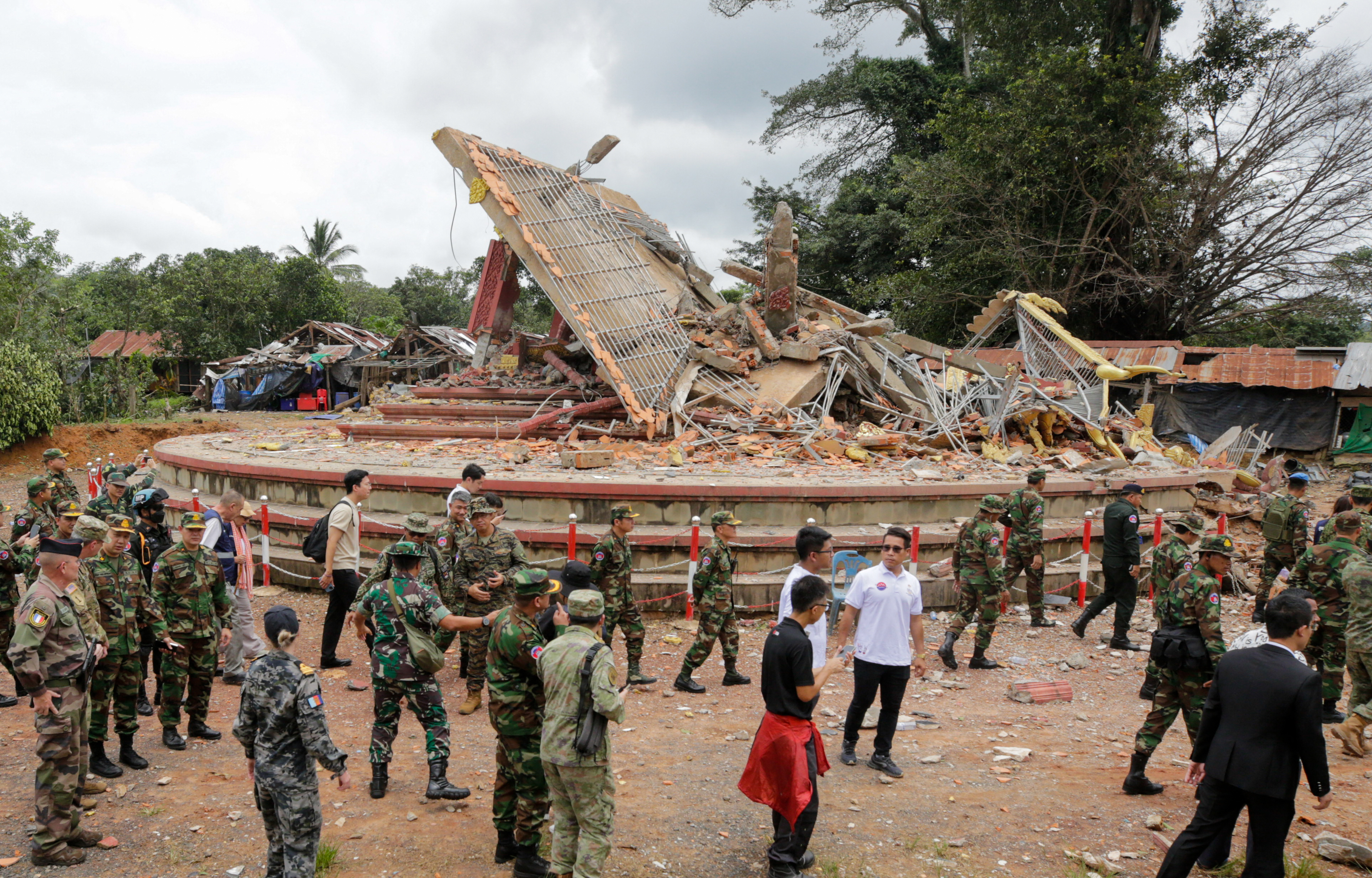 Military attaches and diplomats from 13 countries observe the implementation of the Cambodia-Thailand ceasefire agreement next to a destroyed building.