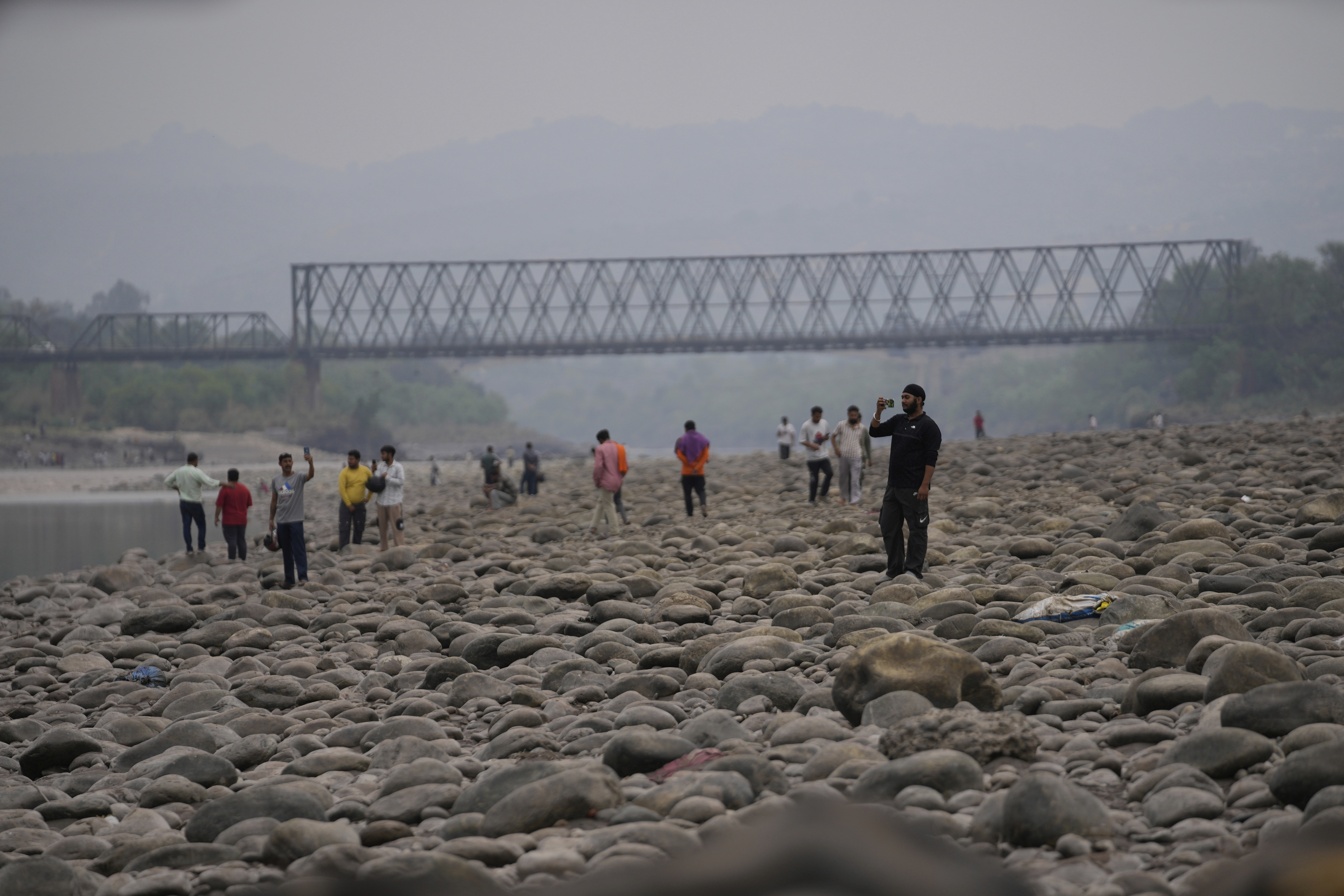 People take photograph on the dry Cheneb river after the flow of water was halted from a dam, at Akhnoor, on the outskirts of Jammu, India, Monday, May 5, 2025. (AP Photo/Channi Anand)
