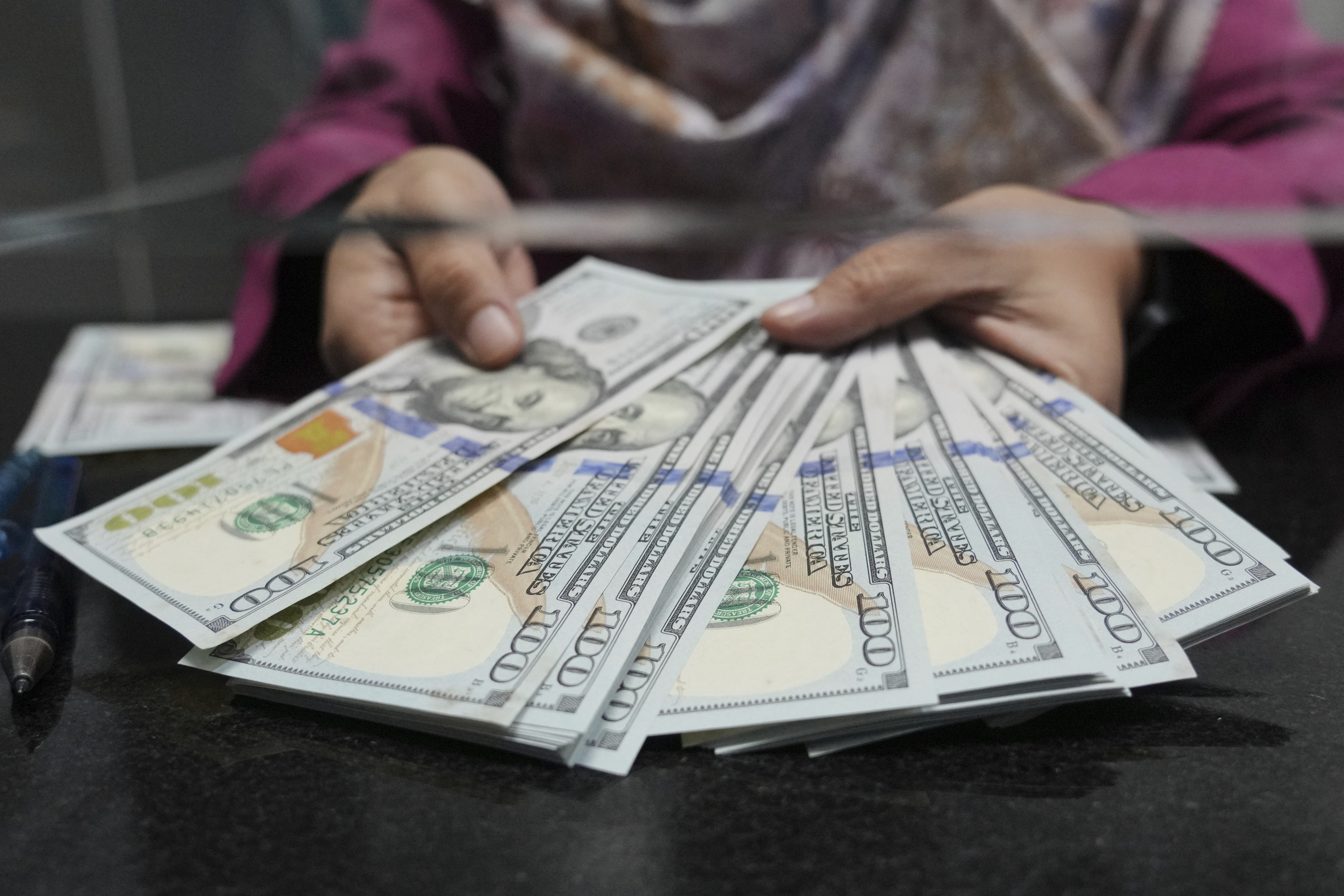 An employee shows US dollar bills at a money changer in Jakarta, Indonesia, Wednesday, July 16, 2025. (AP Photo/Tatan Syuflana)
