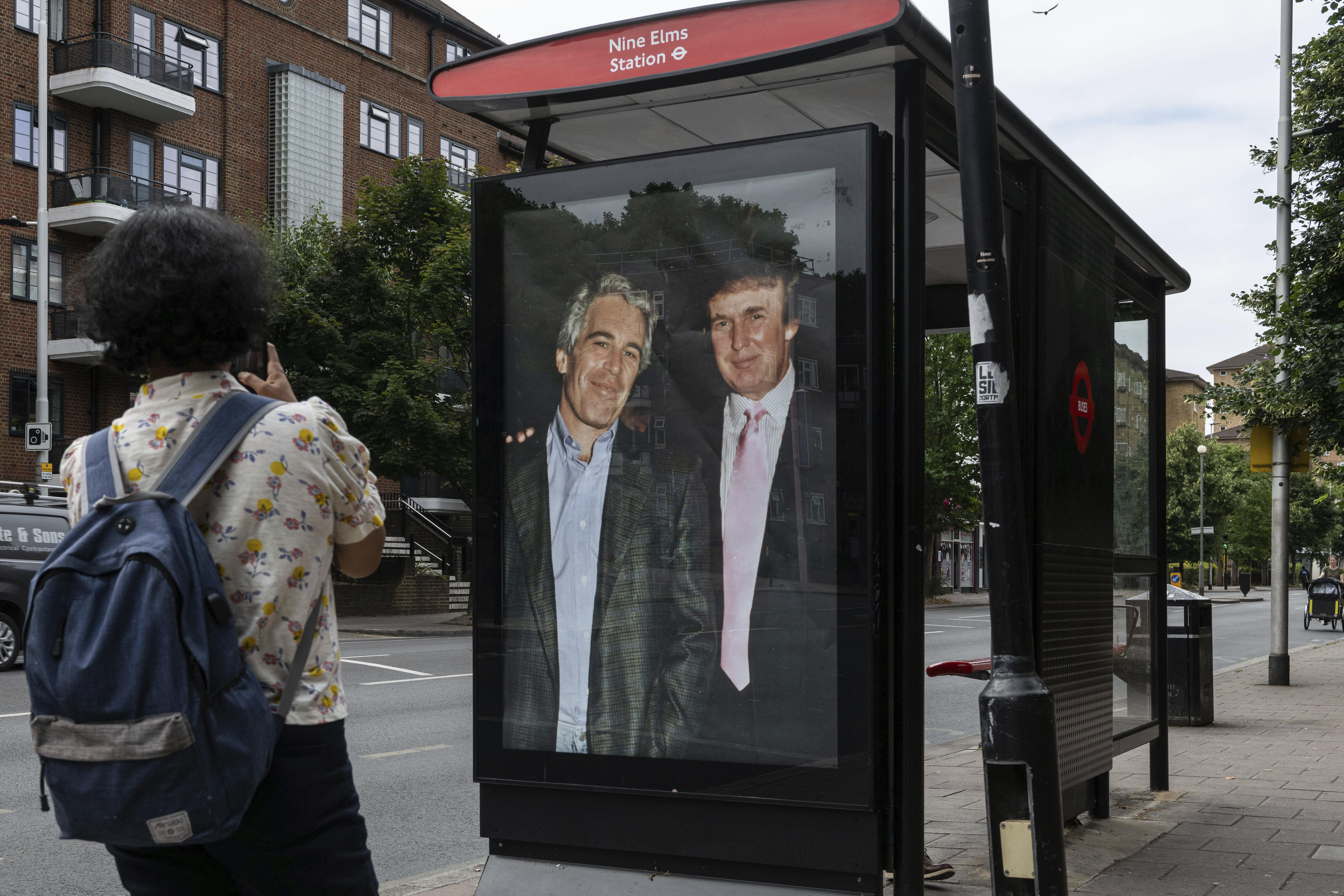 A commuter passes a bus ad in London featuring Donald Trump and Jeffrey Epstein