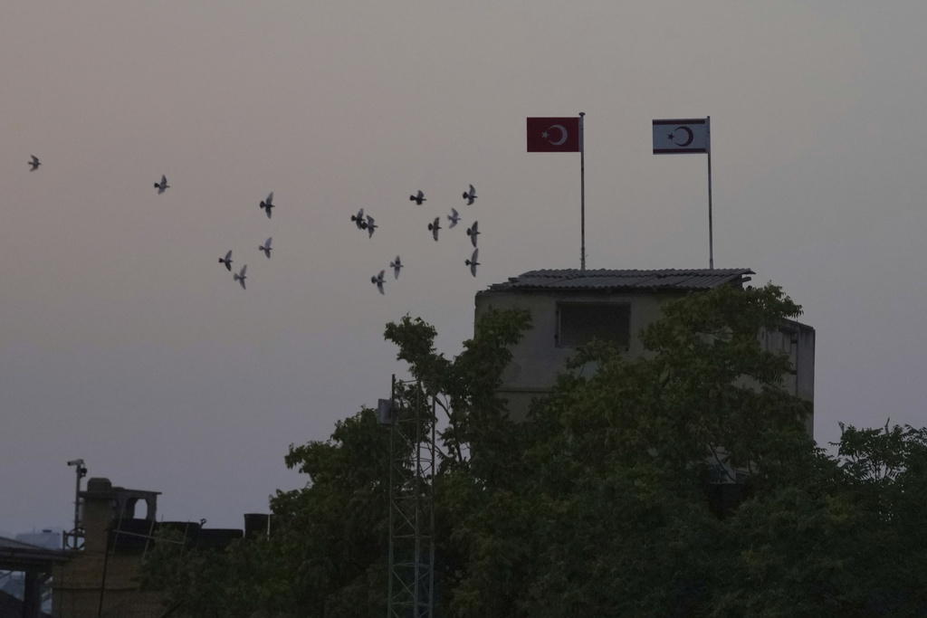 Birds fly behind a Turkish military guard post with a Turkish, left, and Turkish Cypriot breakaway flags.