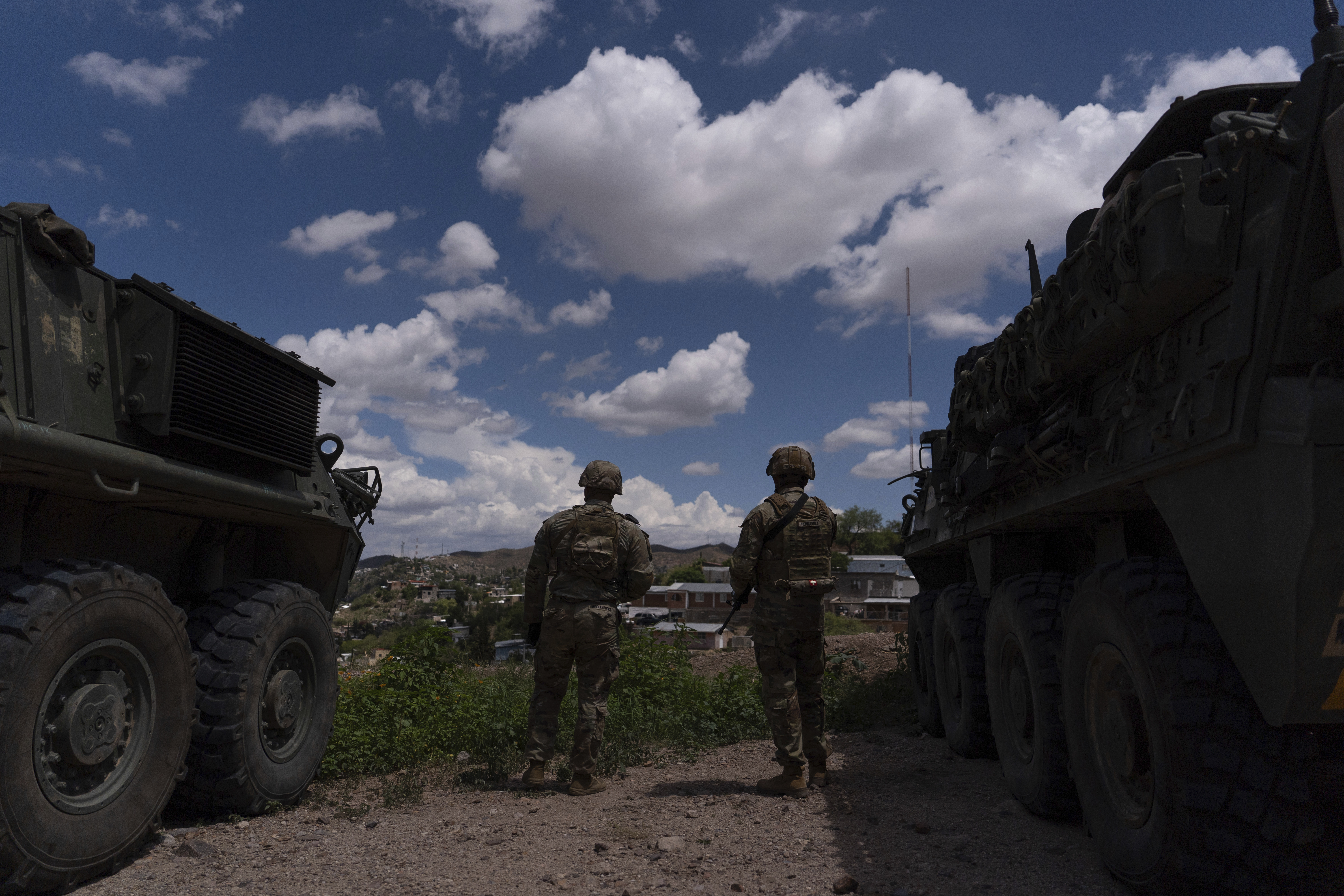 Two US Army soldiers stand between Stryker combat vehicles as they watch over the US-Mexico border fence from a hilltop in Nogales, Arizona, on July 22, 2025. [Jae C Hong/AP Photo]