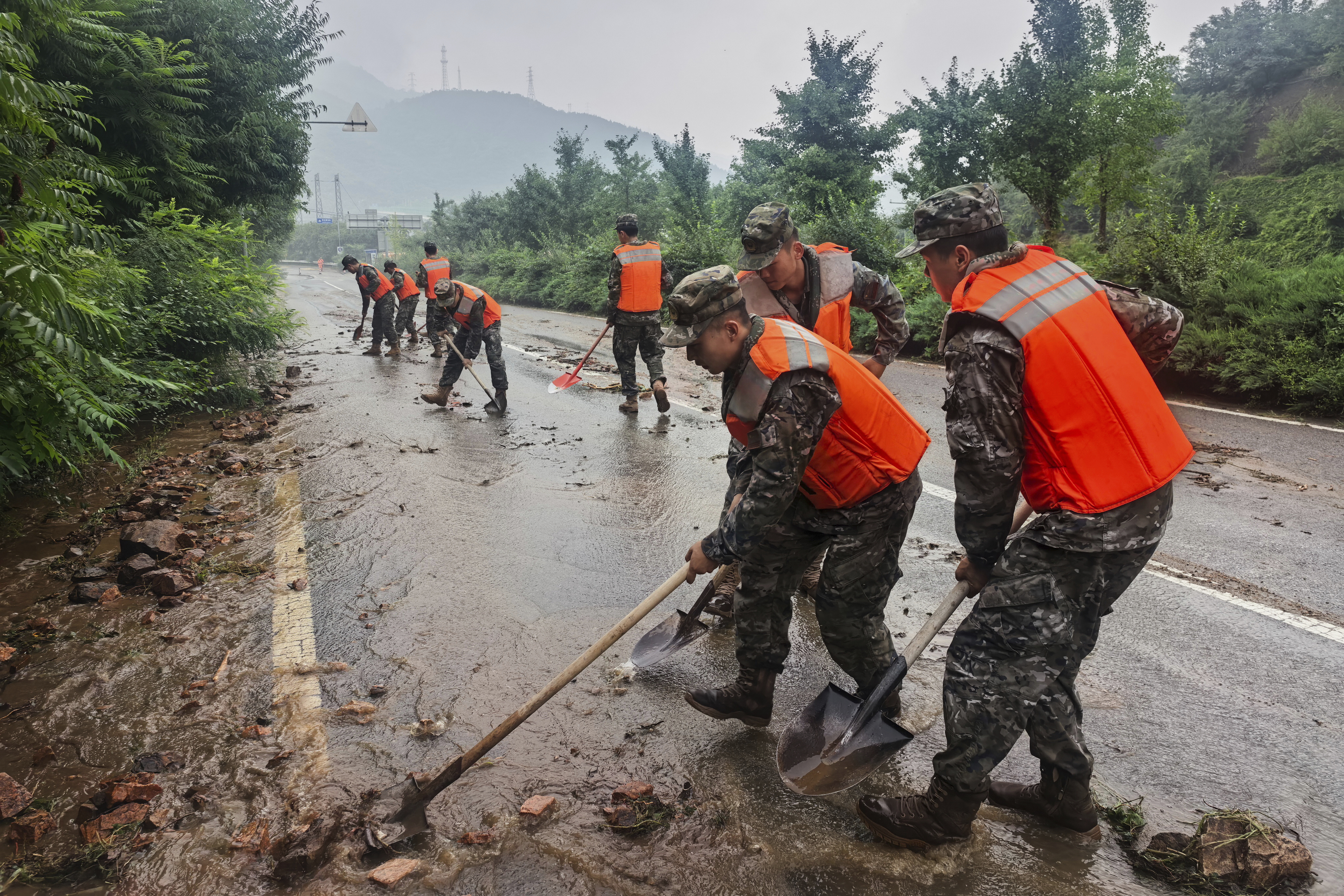 In this photo released by Xinhua News Agency, members of the Chinese People's Armed Police Force clean up silt on a road in Miyun District as continuous rain fall triggers alerts, in north of Beijing on July 27, 2025. (Wang Xiqing/Xinhua via AP)