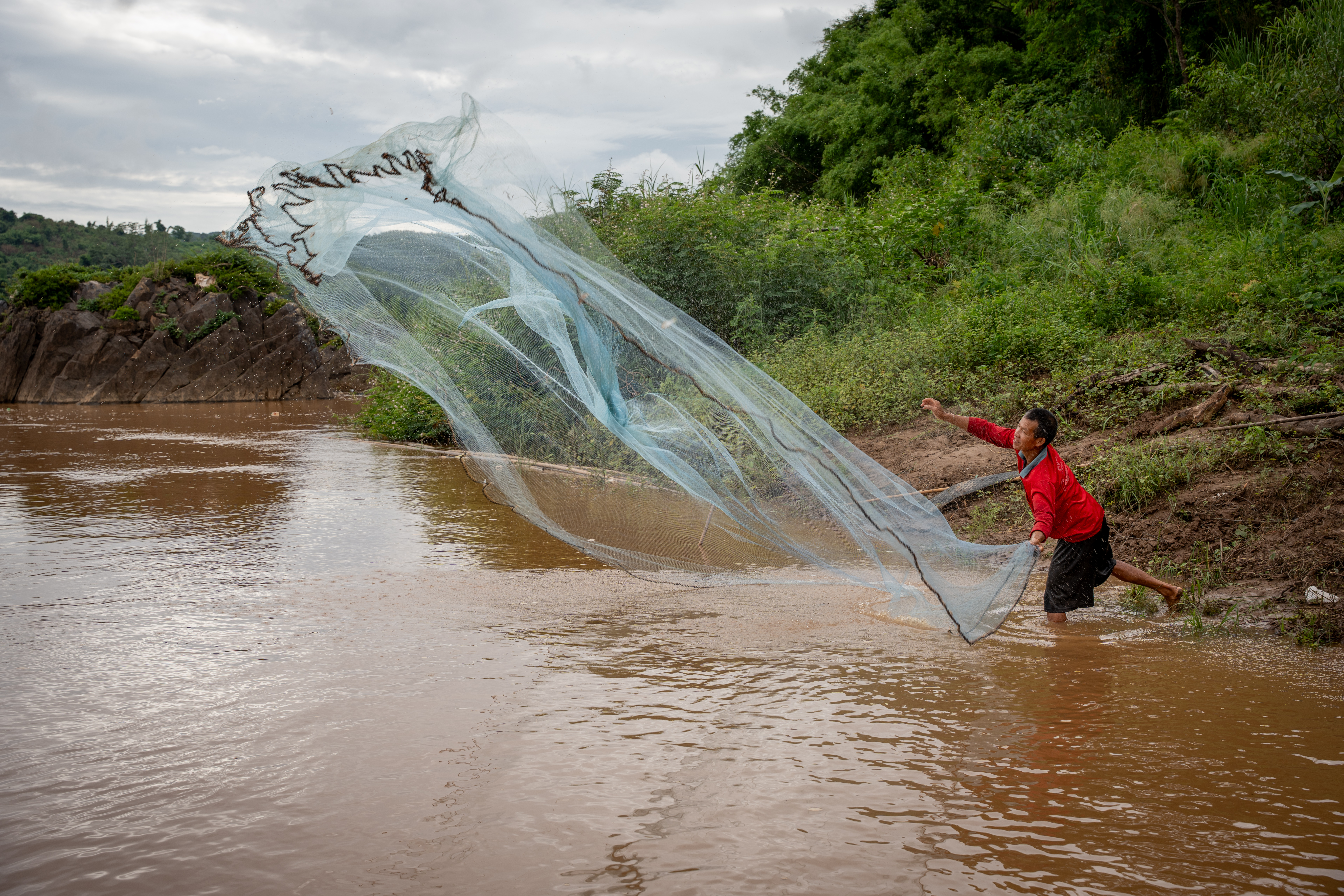 Laotian fisherman Khon, 52, throws a net from the bank of the Mekong River without catching anything [Fabio Polese/Al Jazeera]