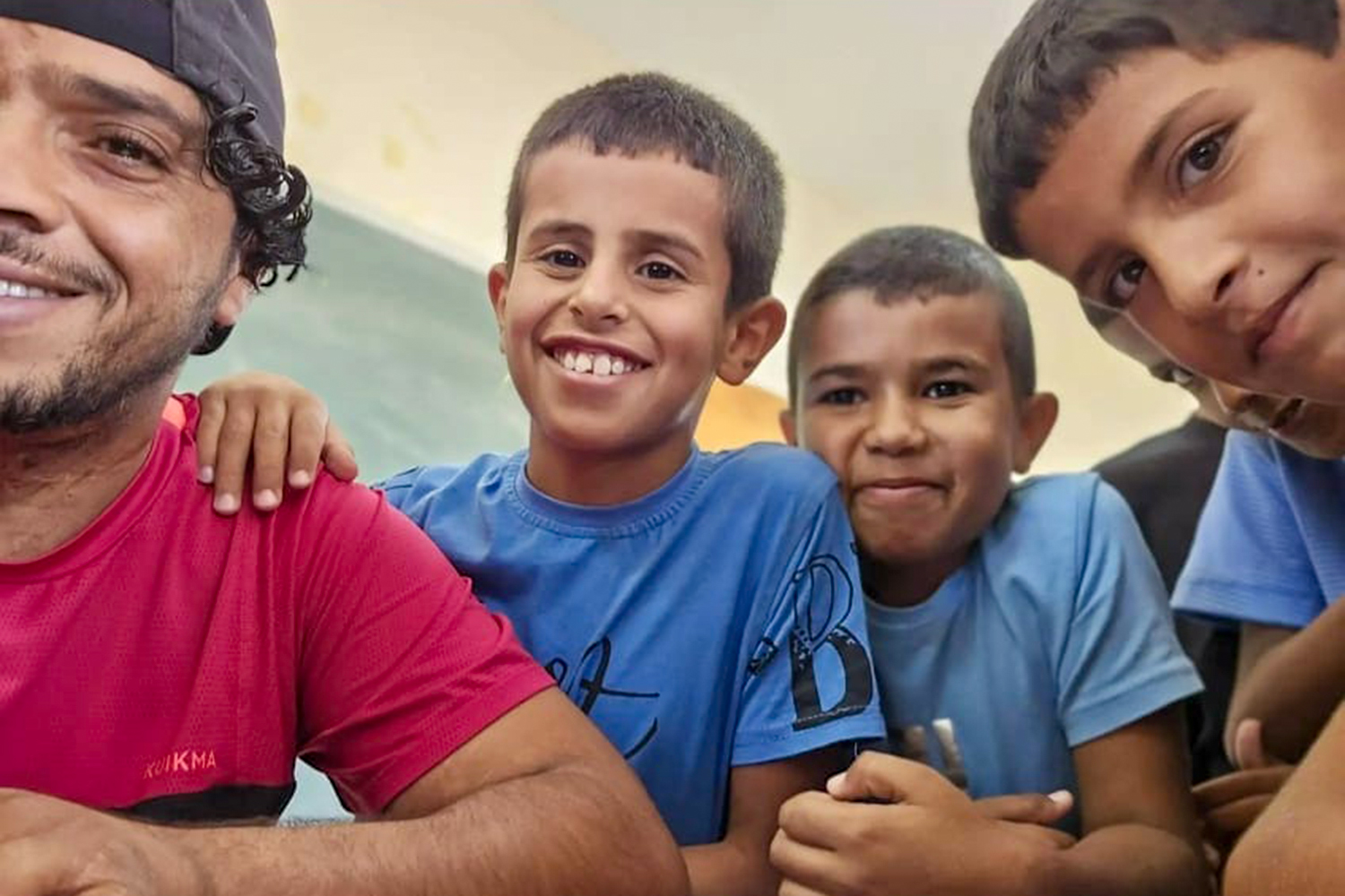 Selfie of a smiling, tanned man with a cap on his head backwards, and three of his smiling students