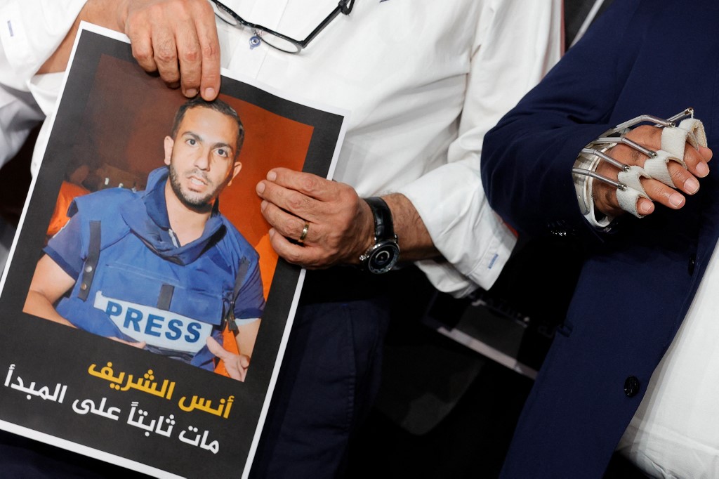 Wael Al-Dahdouh (R), Al Jazeera's bureau chief in Gaza, stands next to Al Jazeera anchor and presenter Mohamed Krichen (L) as he holds the portrait of Anas al-Sharif during a moment of silence to honour Anas and four other colleagues, killed in an overnight Israeli strike in Gaza City [Karim Jaafar/AFP]