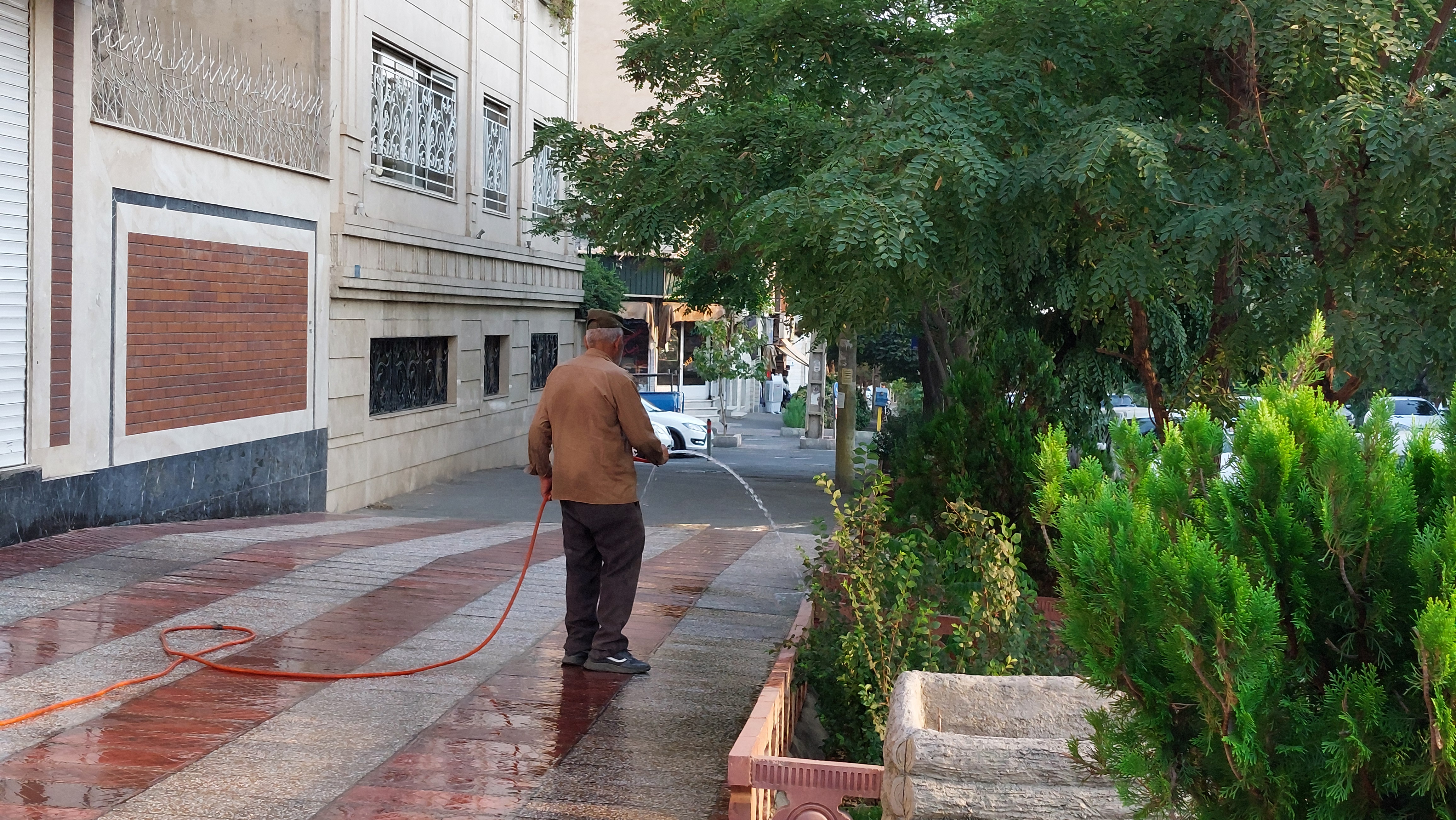 the back of a man holding a hose as he douses the sidewalk
