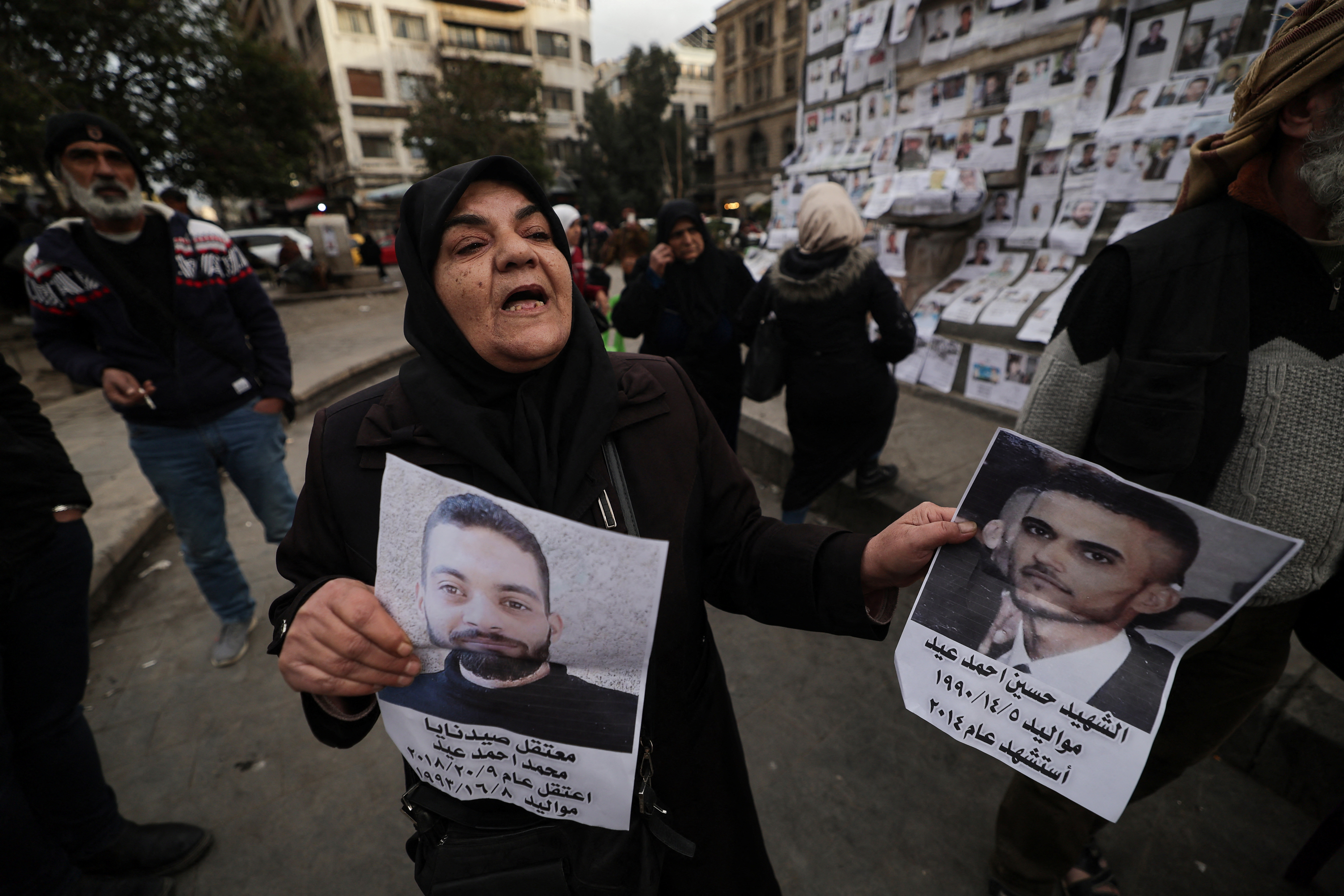 A Syrian woman holds up posters showing her missing sons.