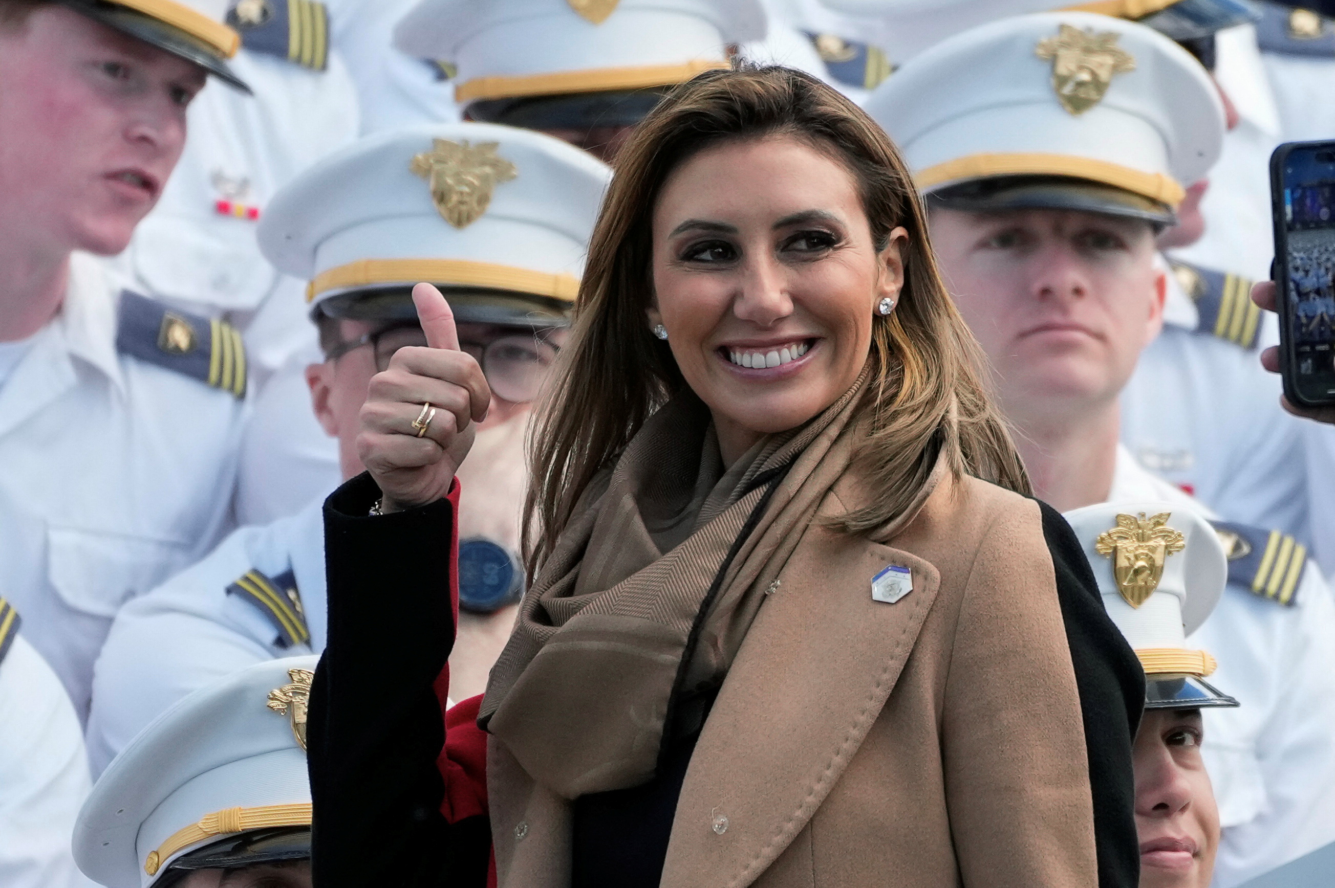 Alina Habba flashes a thumbs-up in front of military officers in dress uniform.