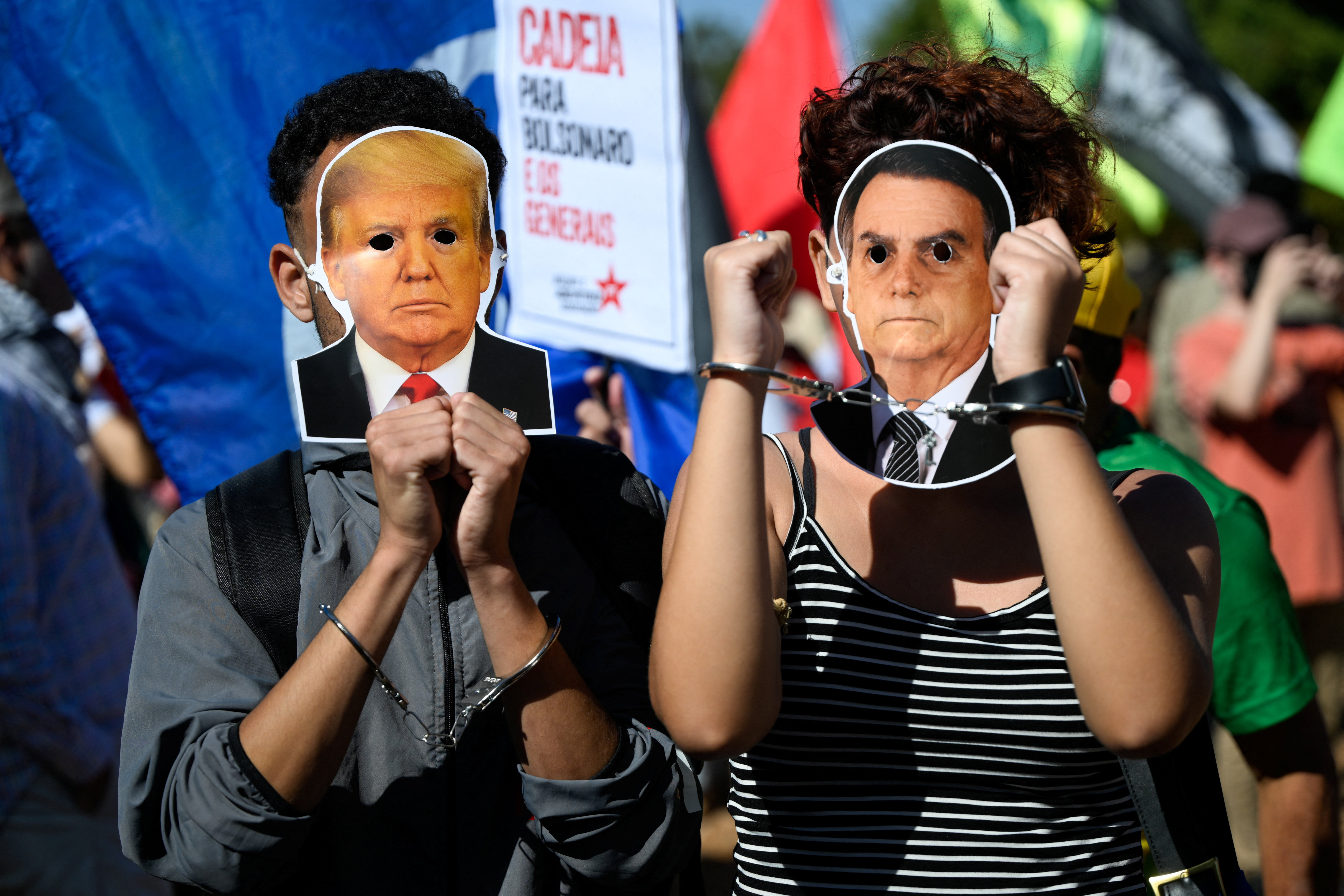 Protesters wear handcuffs and masks of Trump and Jair Bolsonaro over their faces.