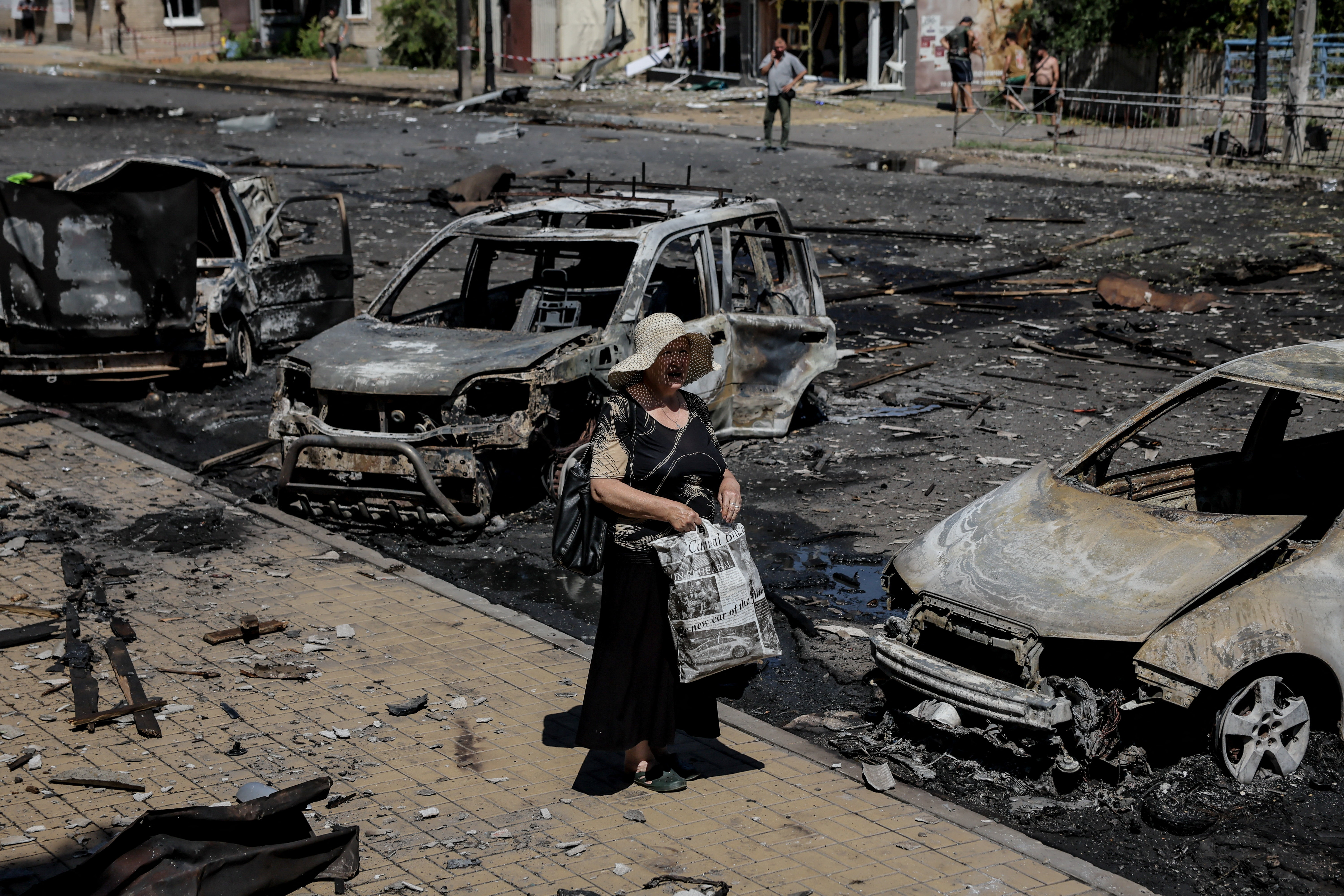 a woman walks between completely burnt out cars
