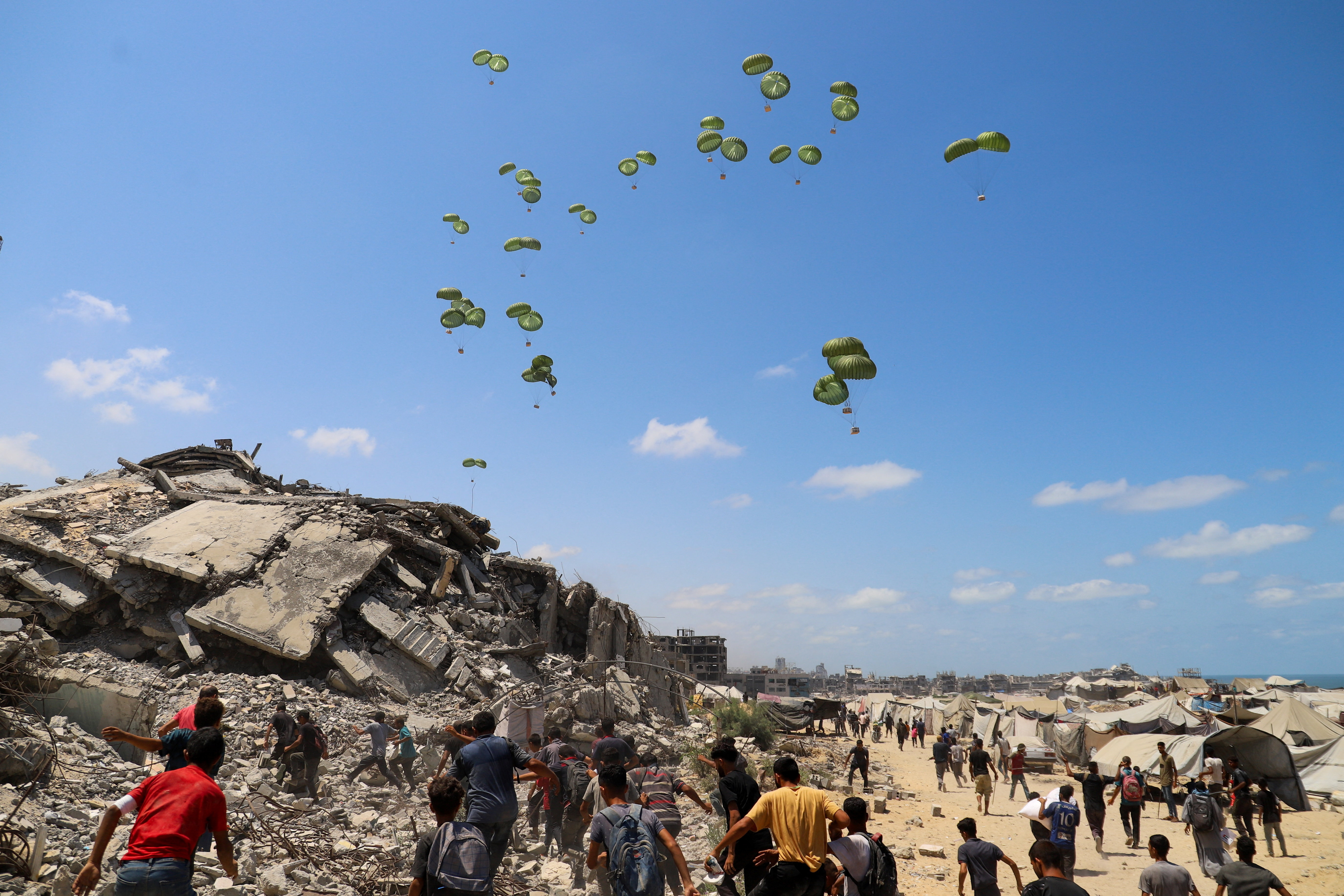Palestinians run towards parachutes carrying aid packages airdropped over northern Gaza Strip
