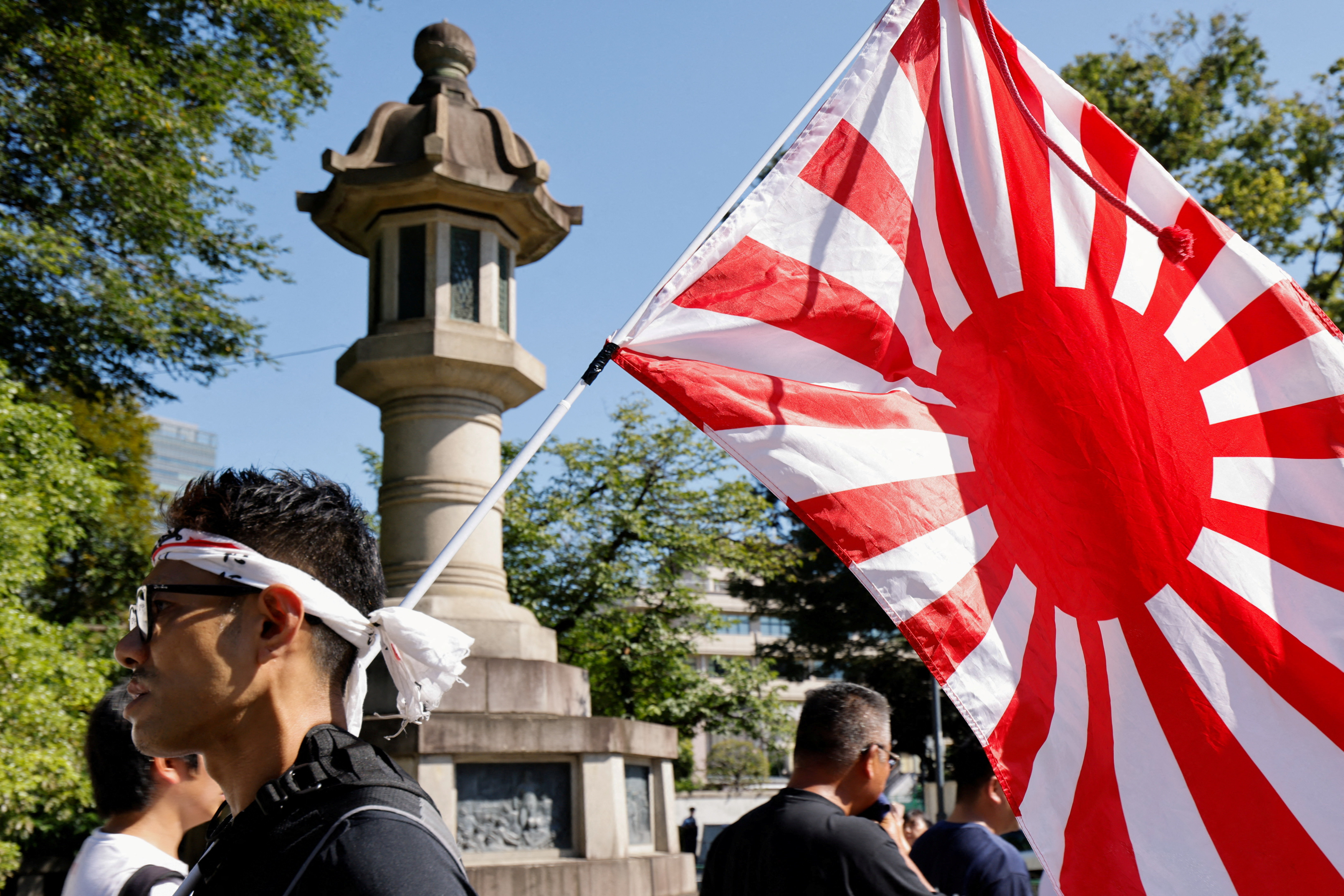 A man displays a Rising Sun flag as people stand in line to pray during their visit to the controversial Yasukuni Shrine, in Tokyo, Japan, on August 15, 2025 [Manami Yamada/Reuters]