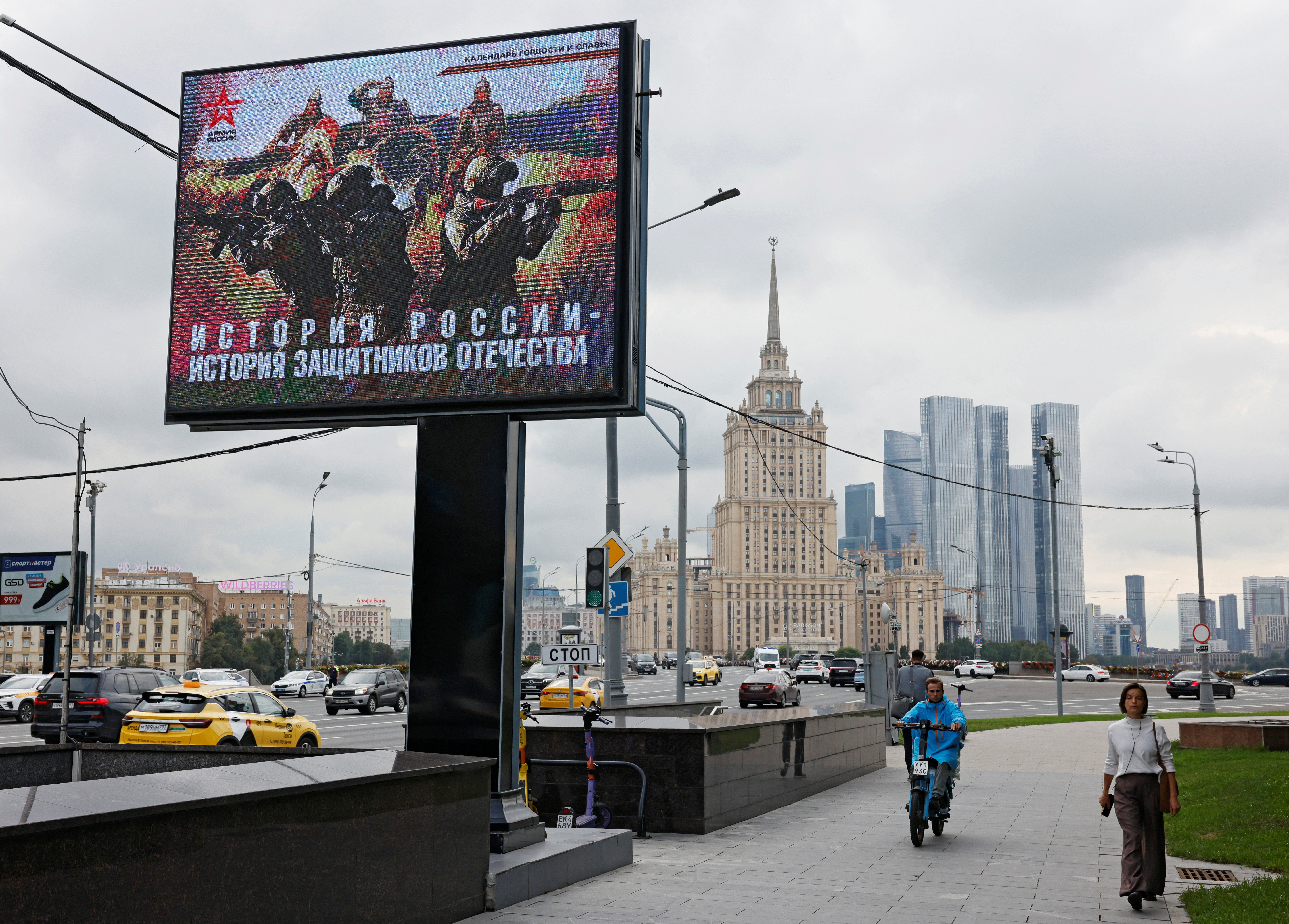 People walk near a banner in support of the Russian army in Moscow, Russia August 11, 2025. The banner reads: "The history of Russia is the history of the defenders of the fatherland". REUTERS/Yulia Morozova