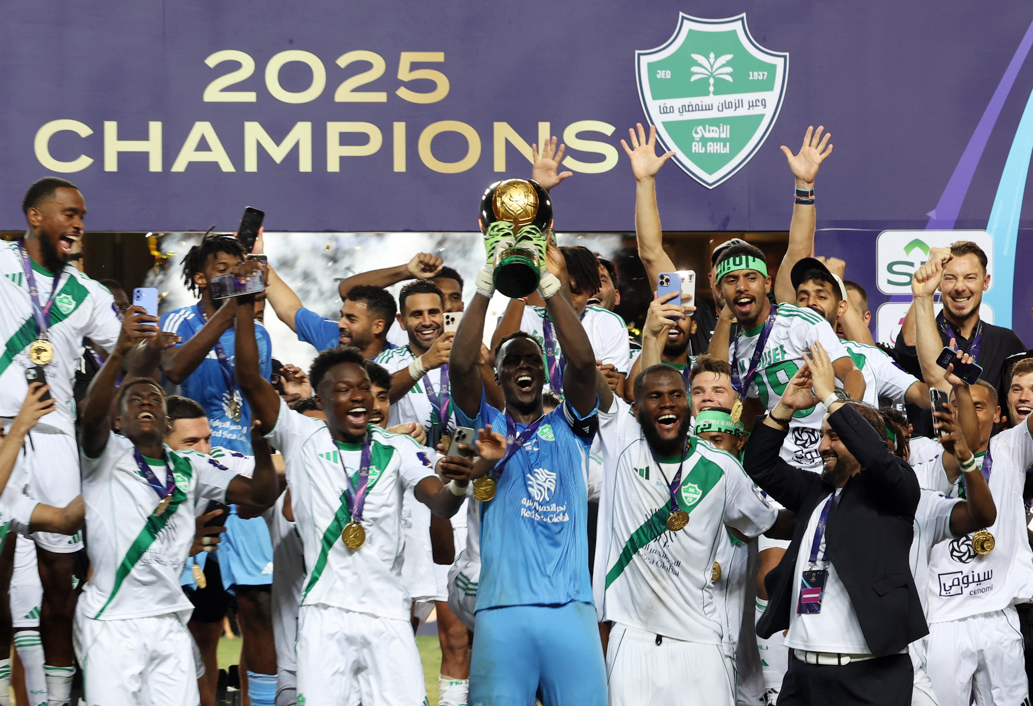 Al Ahli's Edouard Mendy lifts the trophy and celebrates on the podium with Franck Kessie and teammates after winning the Saudi Super Cup