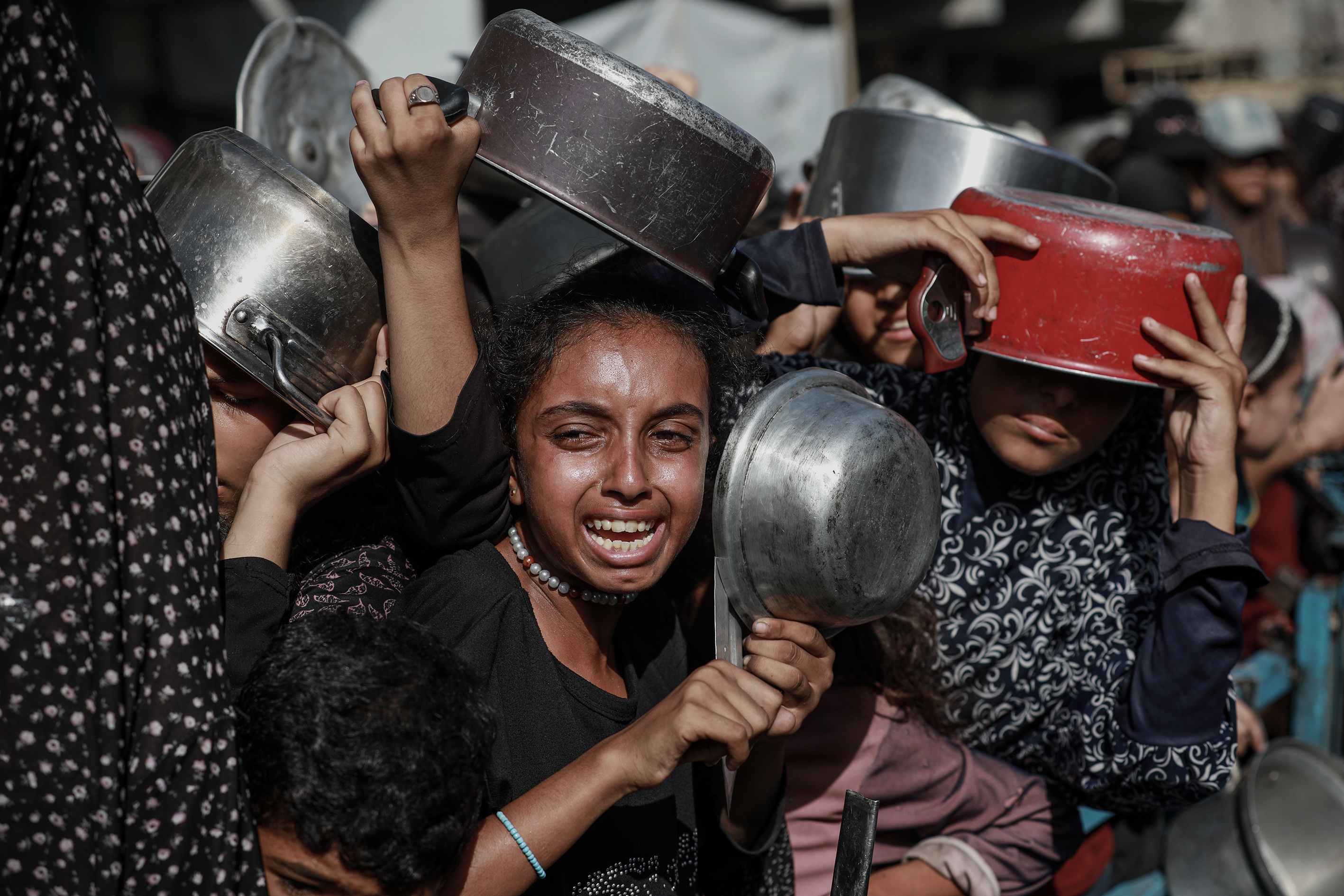 Palestinians, struggling with hunger, form a line to receive hot meals.