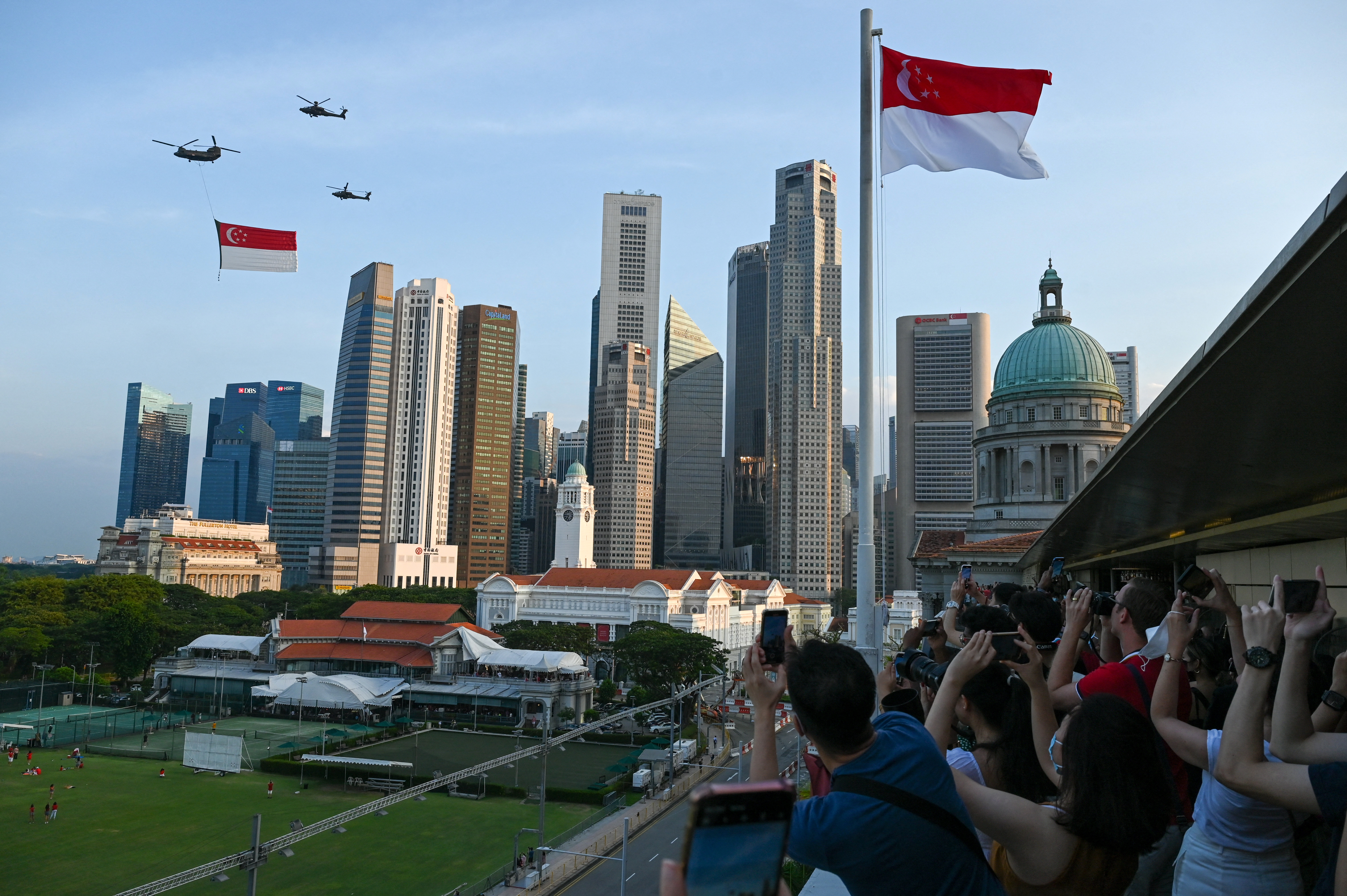 Spectators cheer as a Singapore's Air Force Chinook helicopter escorted by Apache helicopters parade with the flag of Singapore to mark the country's 57th National Day, in Singapore on August 9, 2022. (Photo by Roslan RAHMAN / AFP)