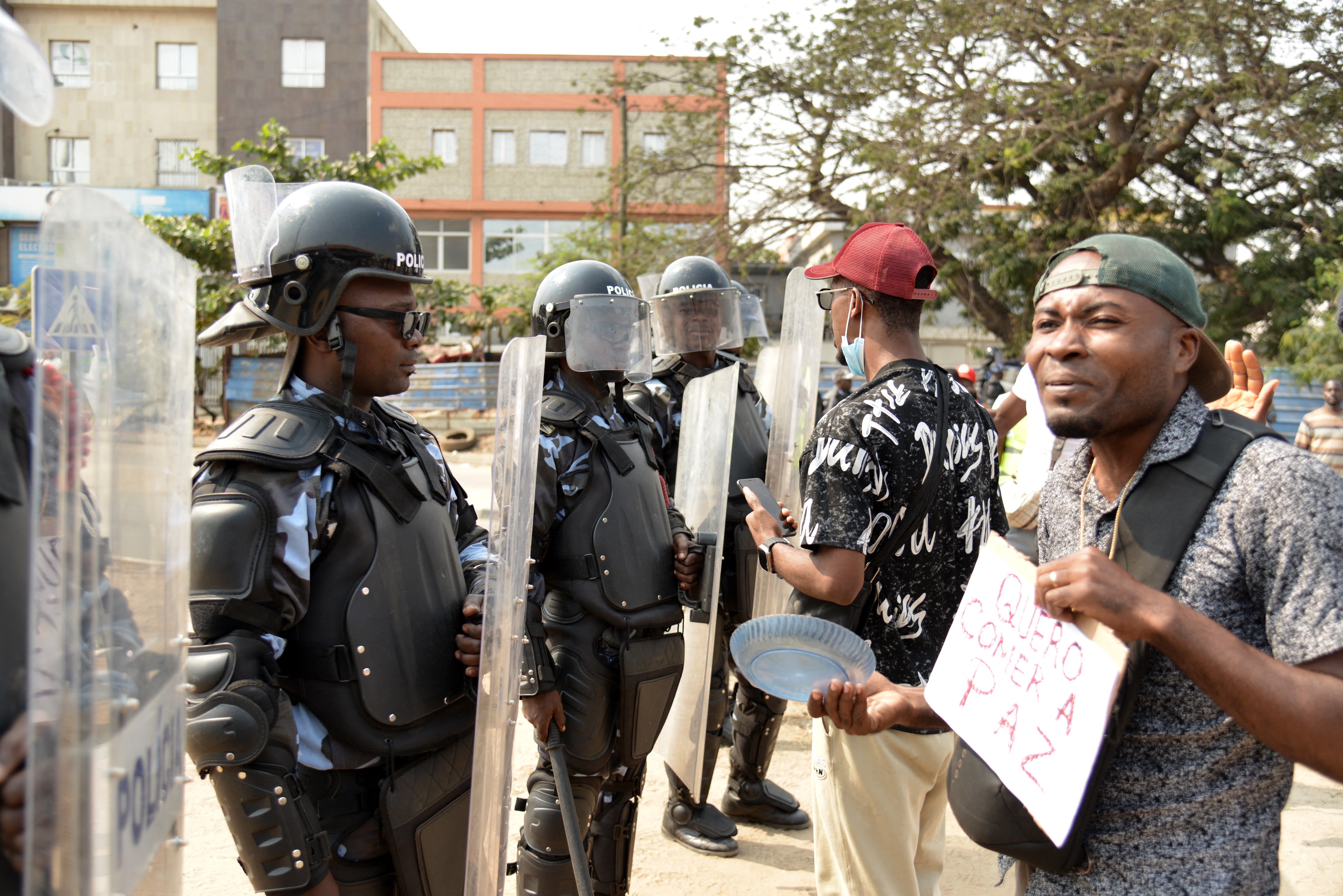 A protester holding a placard approaches Angola anti-riot police officers standing in formation in Luanda in July, 2025 during a protest over high living costs [File: Julio Pacheco Ntela/AFP]