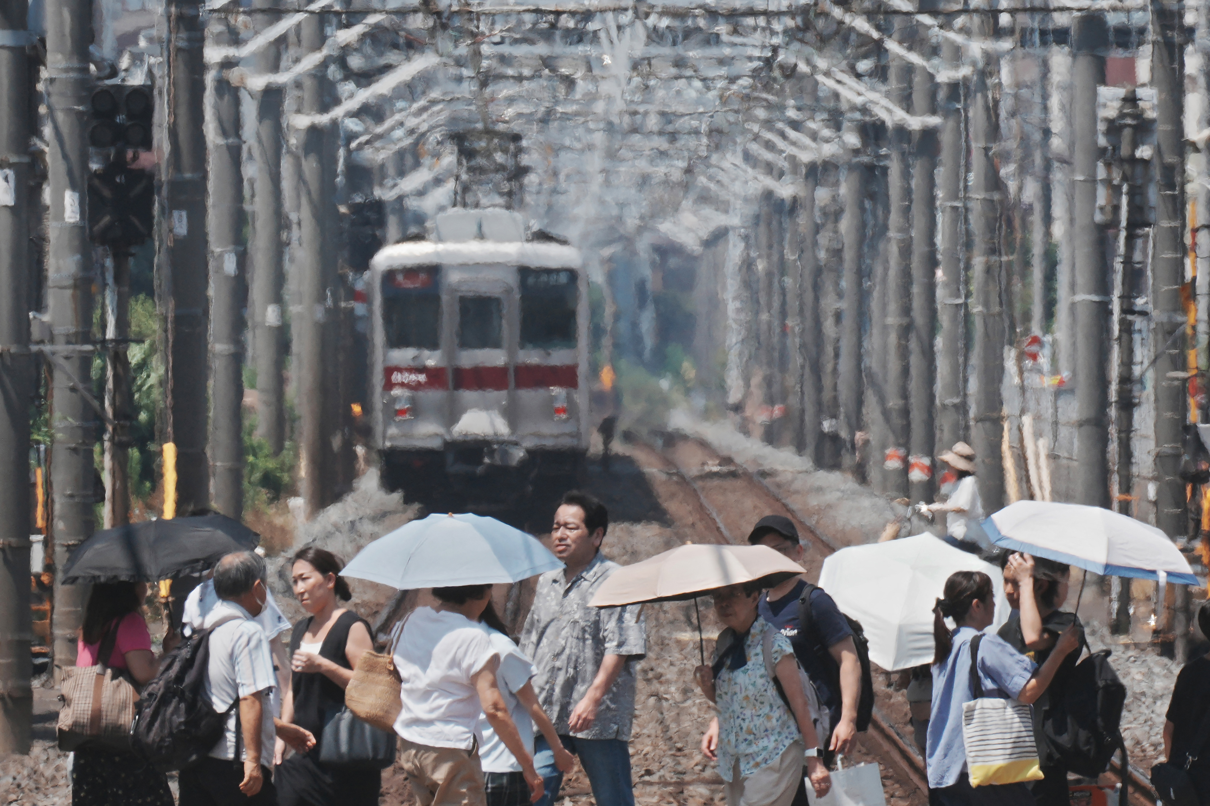 Heat haze is seen in the background while pedestrians with umbrellas cross a railroad track on a hot day in Tokyo, Japan on August 5, 2025.