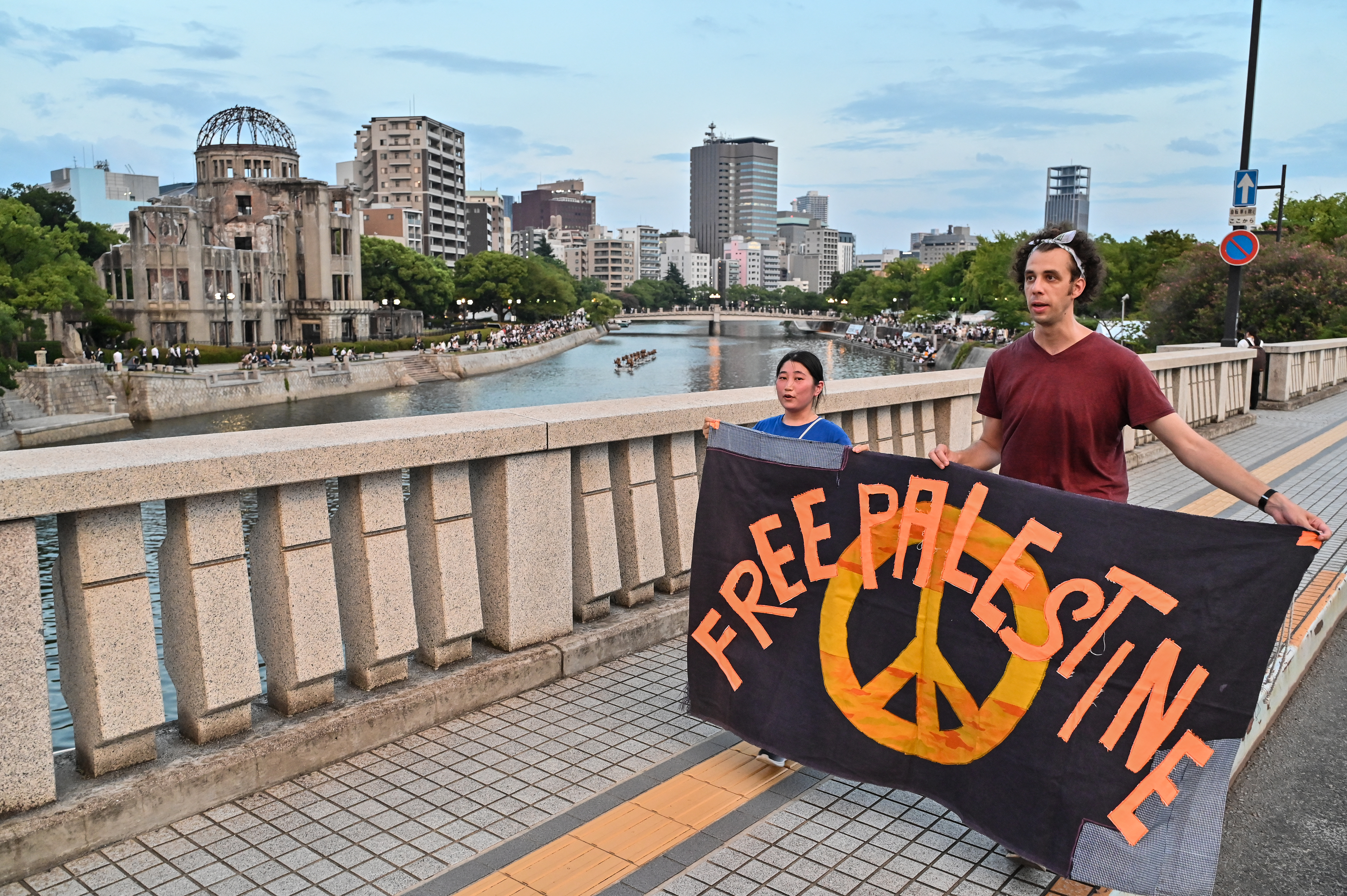 people hold a banner that says free Palestine with the Hiroshima memorial in the background