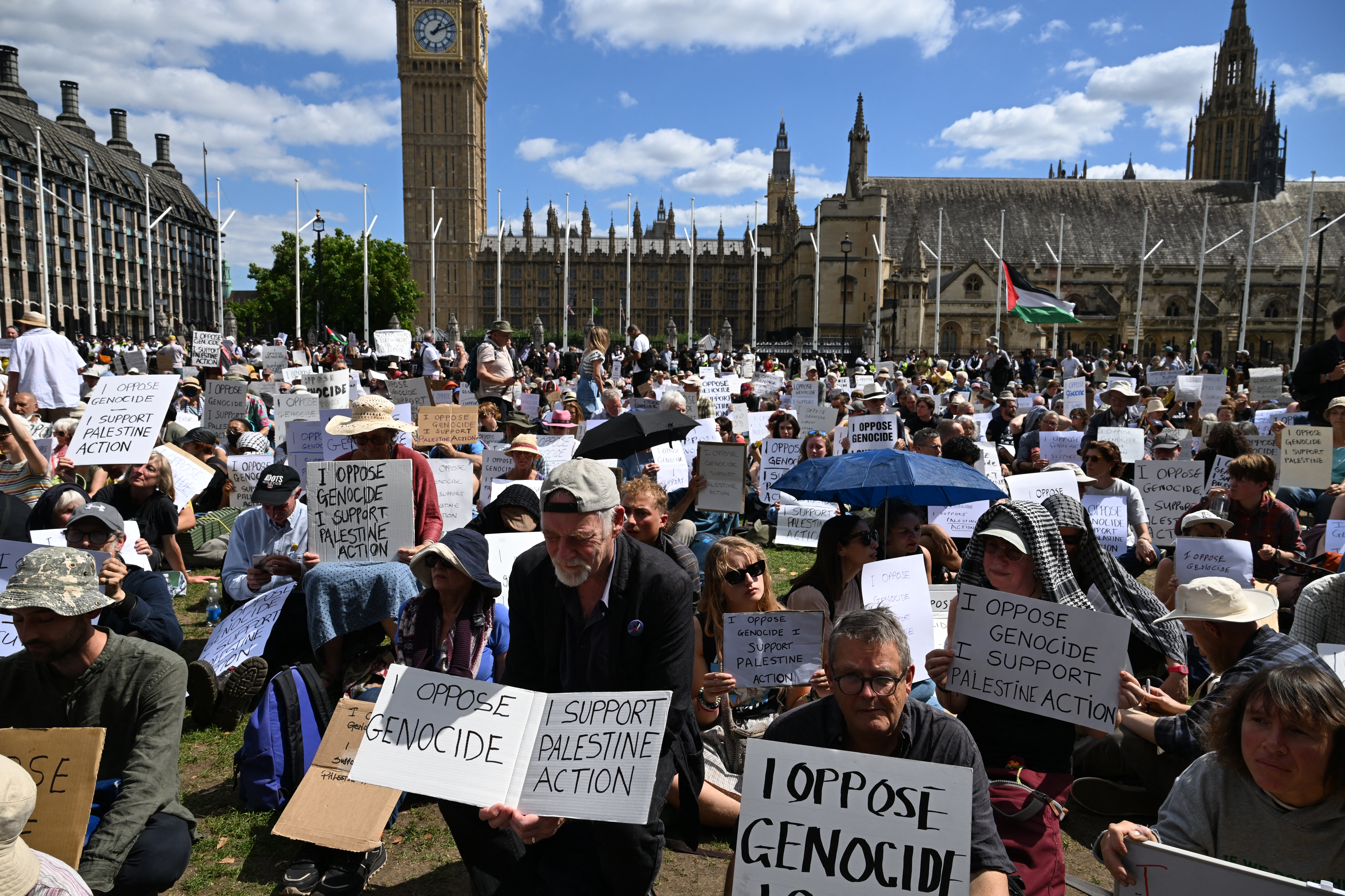 people sit holding protest signs in front of the UK parliament