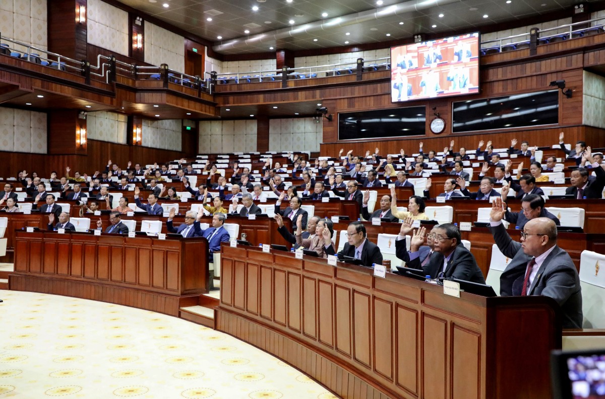 Members of parliament raising their hands during a meeting to pass laws.