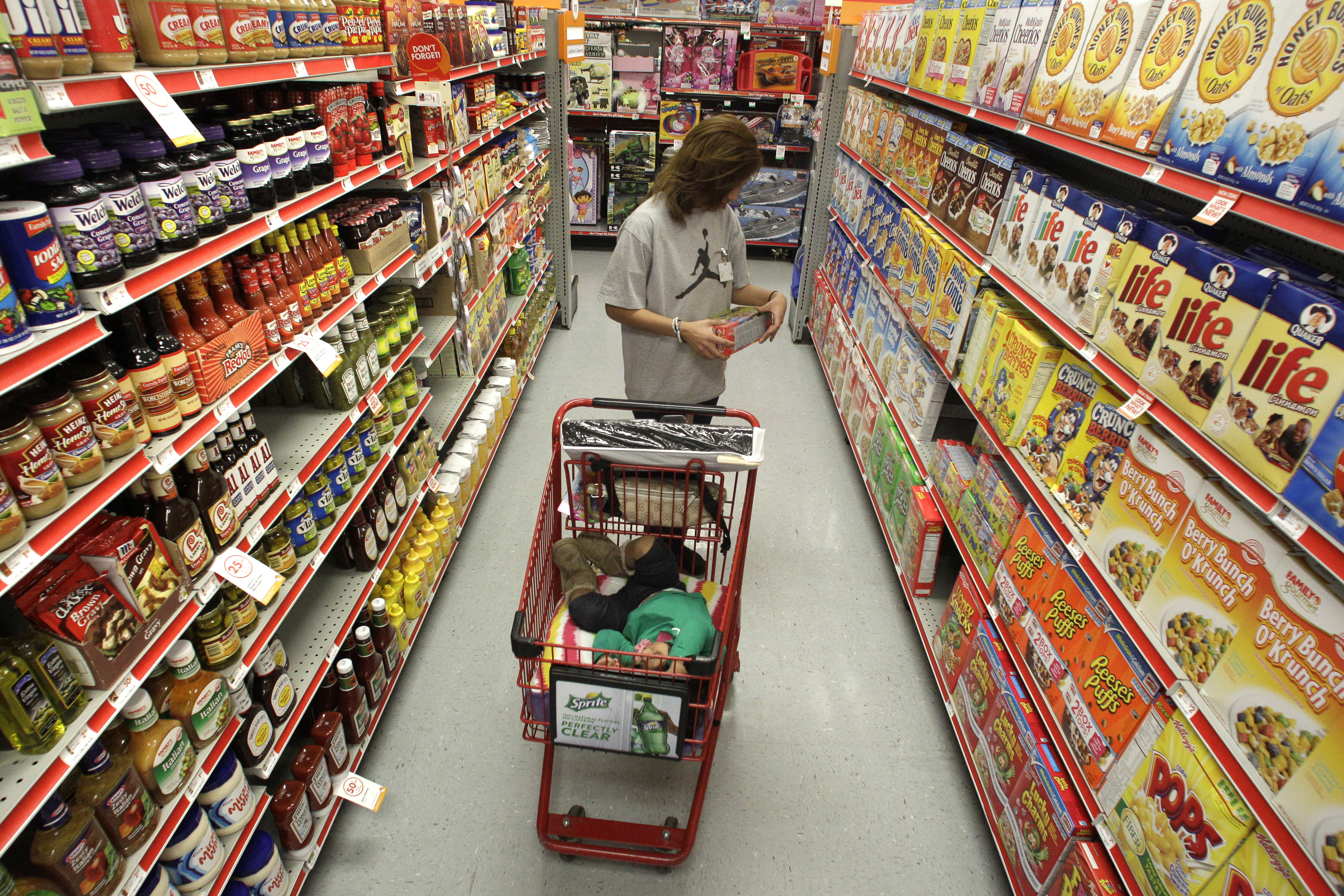 A shopper pushes a cart through an aisle of food at a grocery store.
