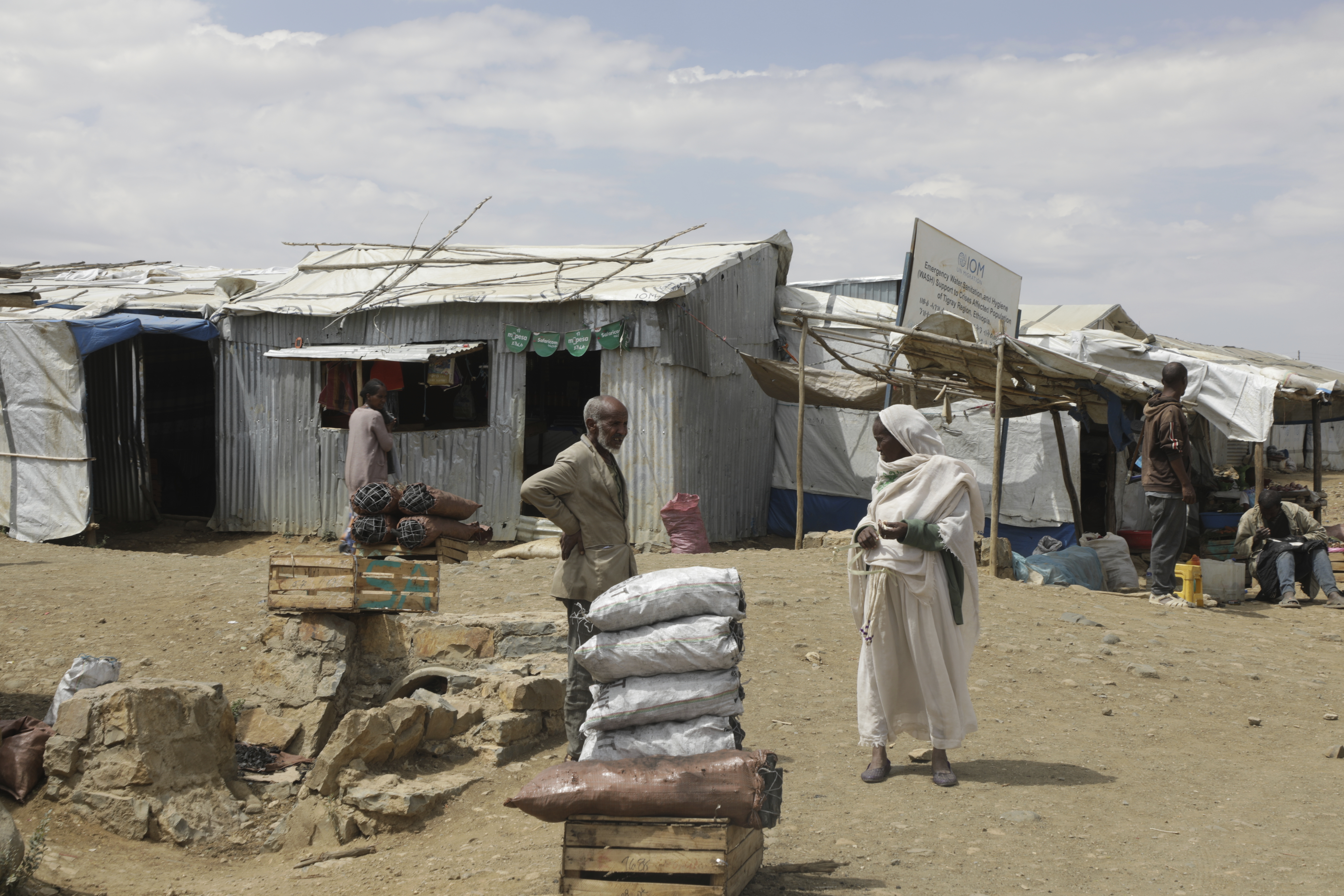 Two displaced people stand in front of food aid sacks in a camp on the outskirts of Tigray