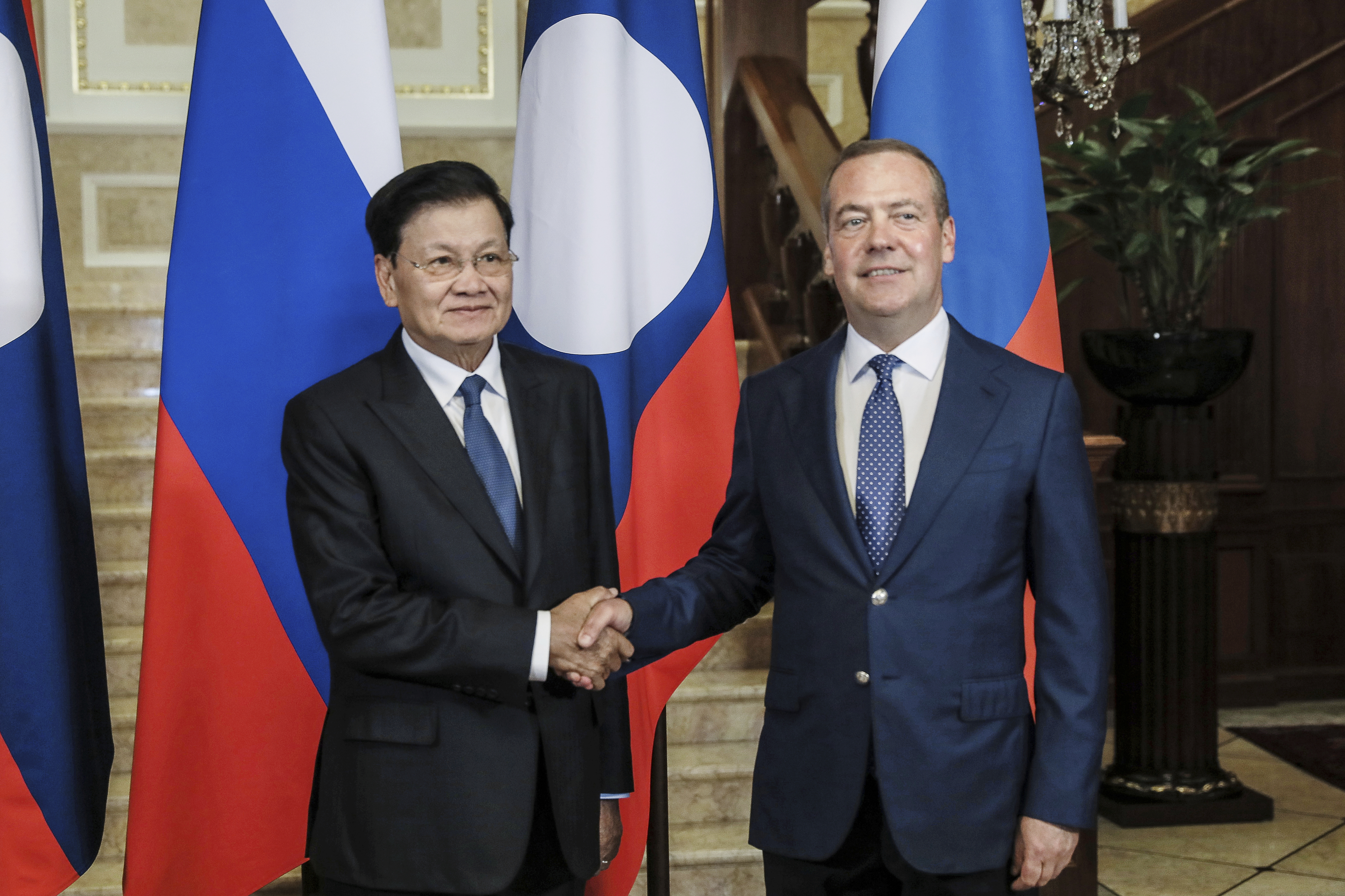 Thongloun Sisoulith shakes hands with Dmitry Medvedev in front of their countries' flags.