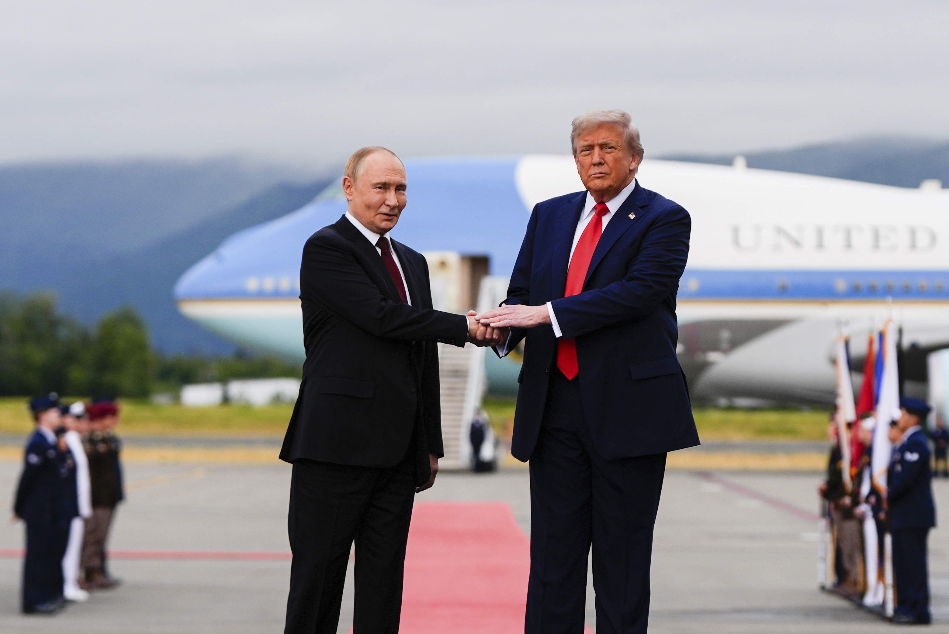 Trump and Putin shake hands on a red carpet leading from Air Force One.