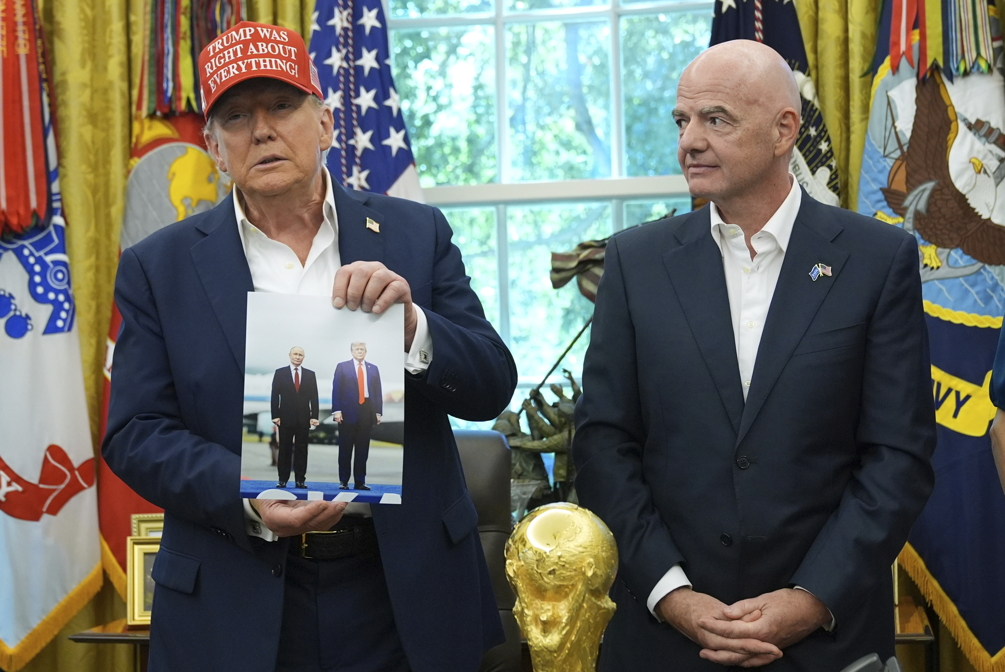 Trump holds up a photograph of himself and Putin while standing next to Gianni Infantino in the Oval Office.
