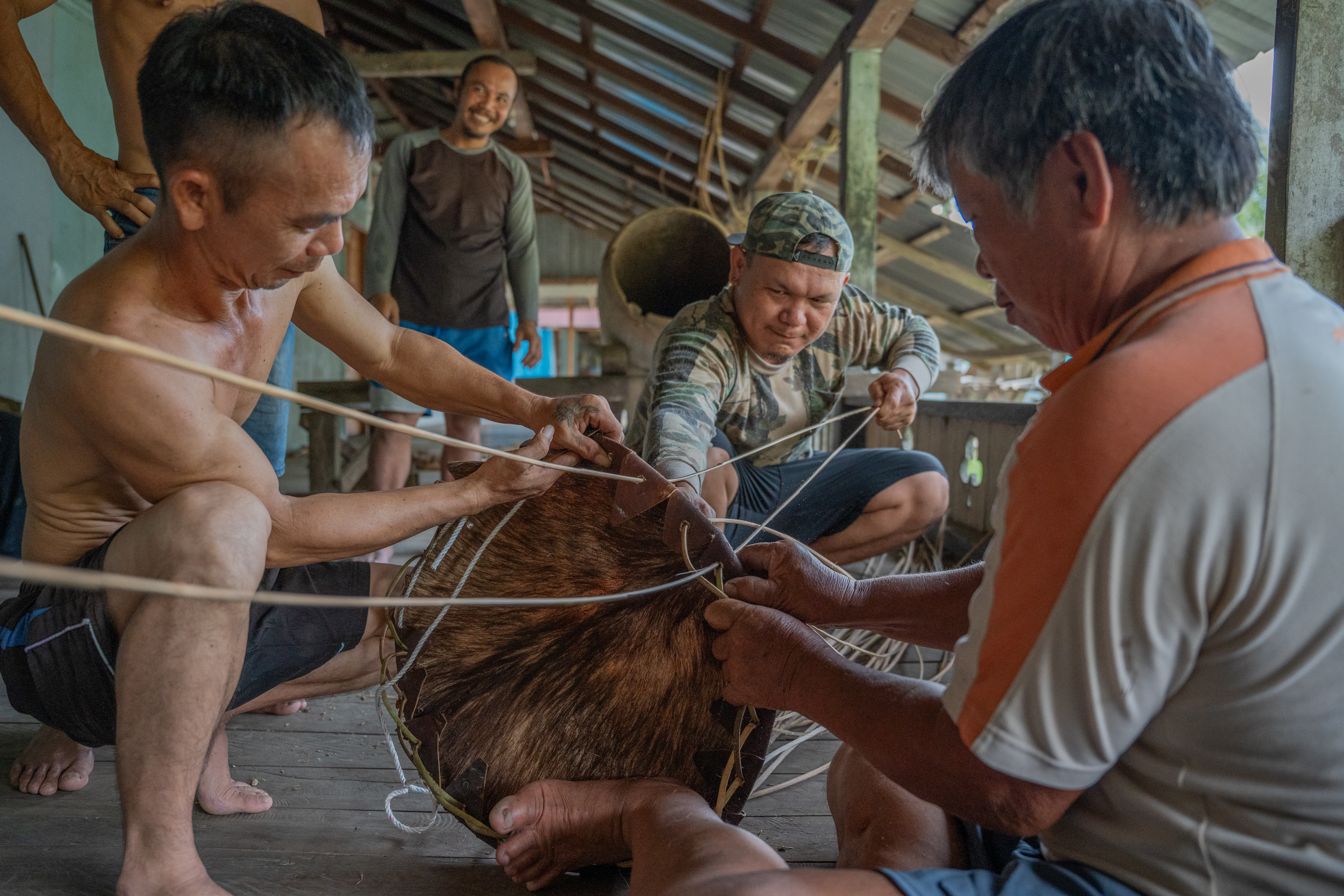 Community members in Long Moh fix an old drum with deer skin. Music has spiritual significance for this Kenyah community [Izzy Sasada/Al Jazeera]