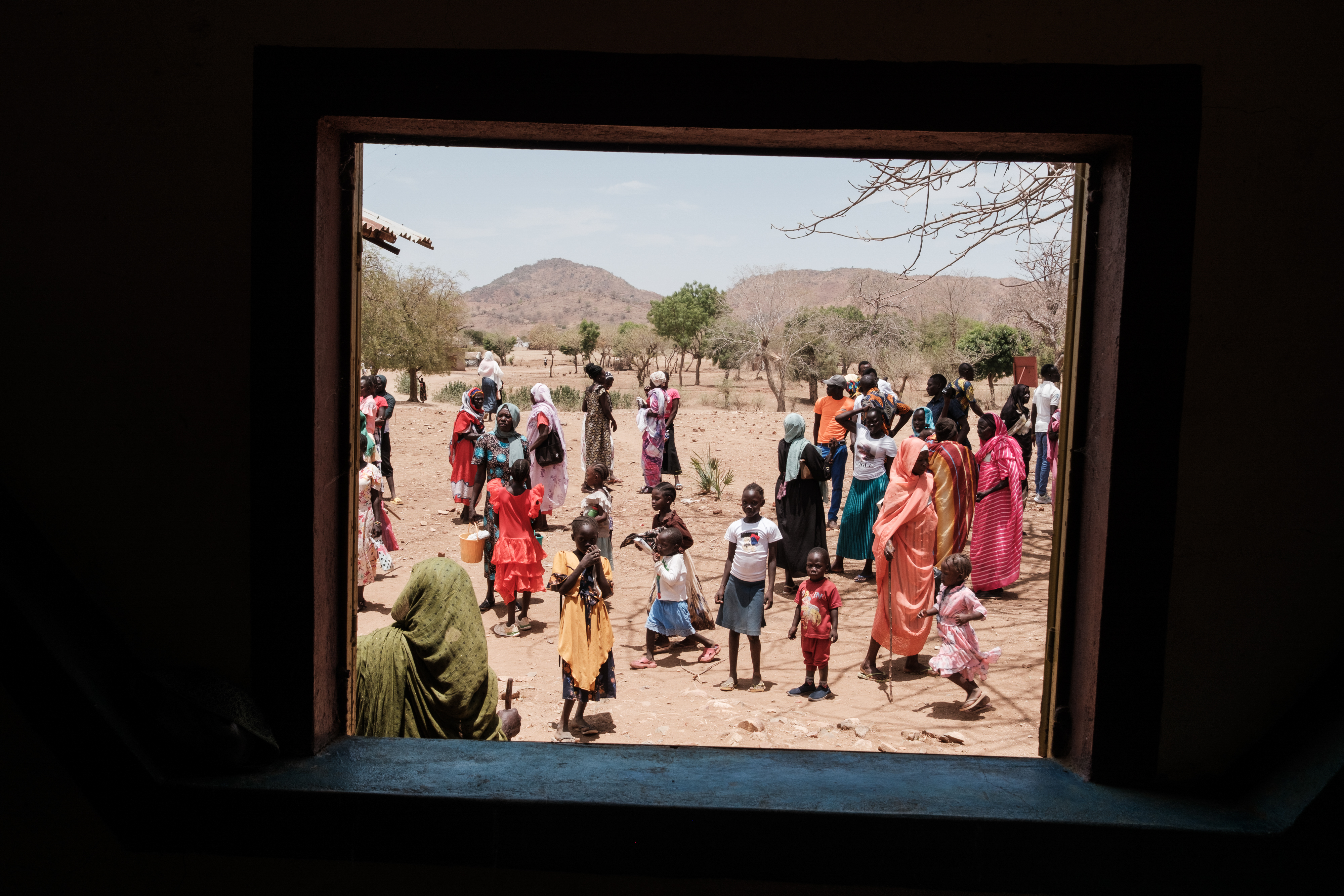 A group of worshippers dressed in bright colours are seen through a church window, with the mountains in the background