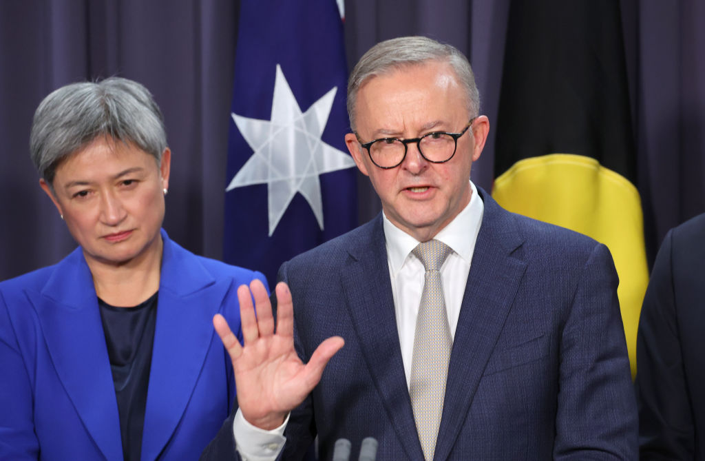 a woman and a man wearing blue suits stand in front of an Australian and an Aboriginal flag