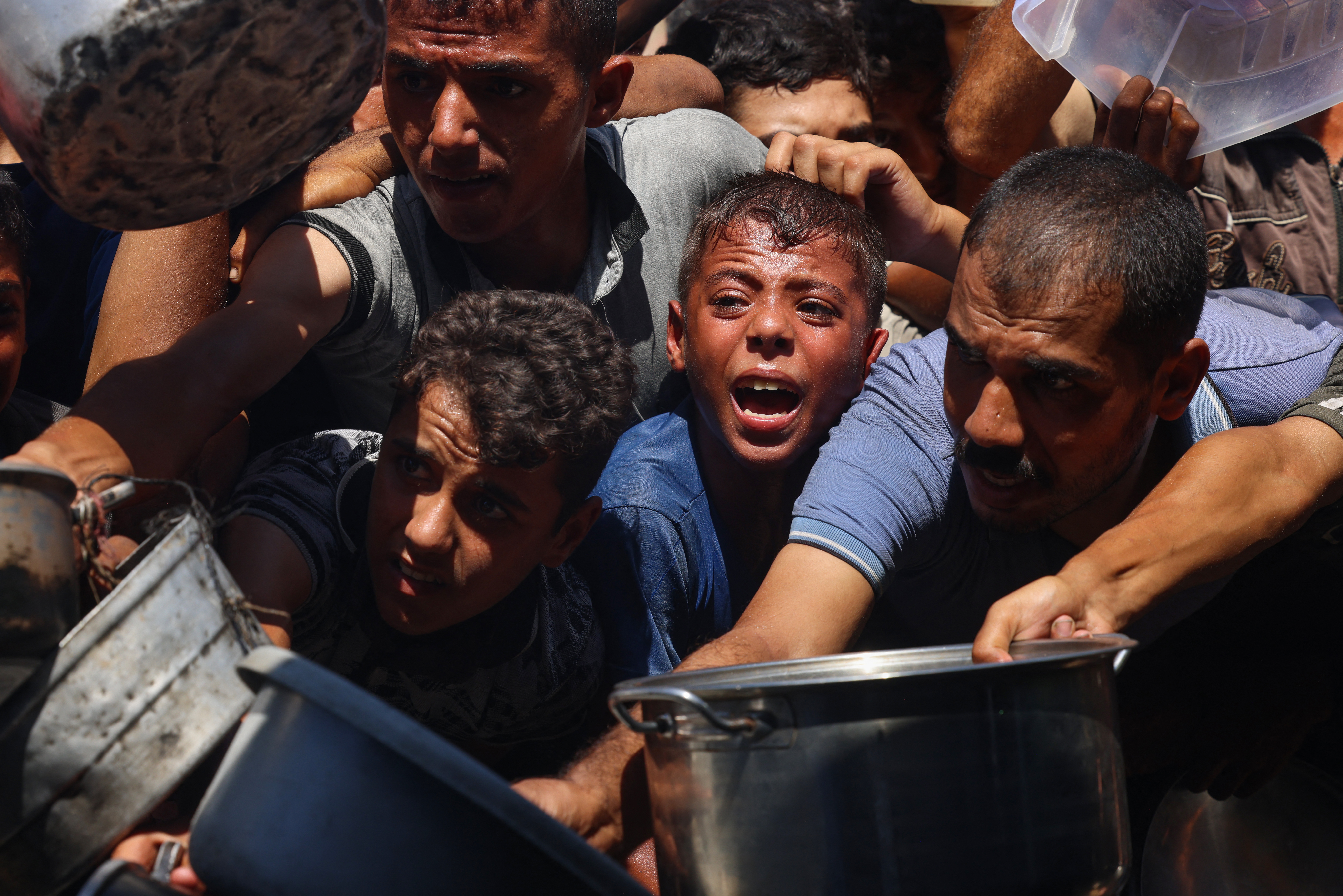 Palestinians shove to receive food portions from a charity kitchen.