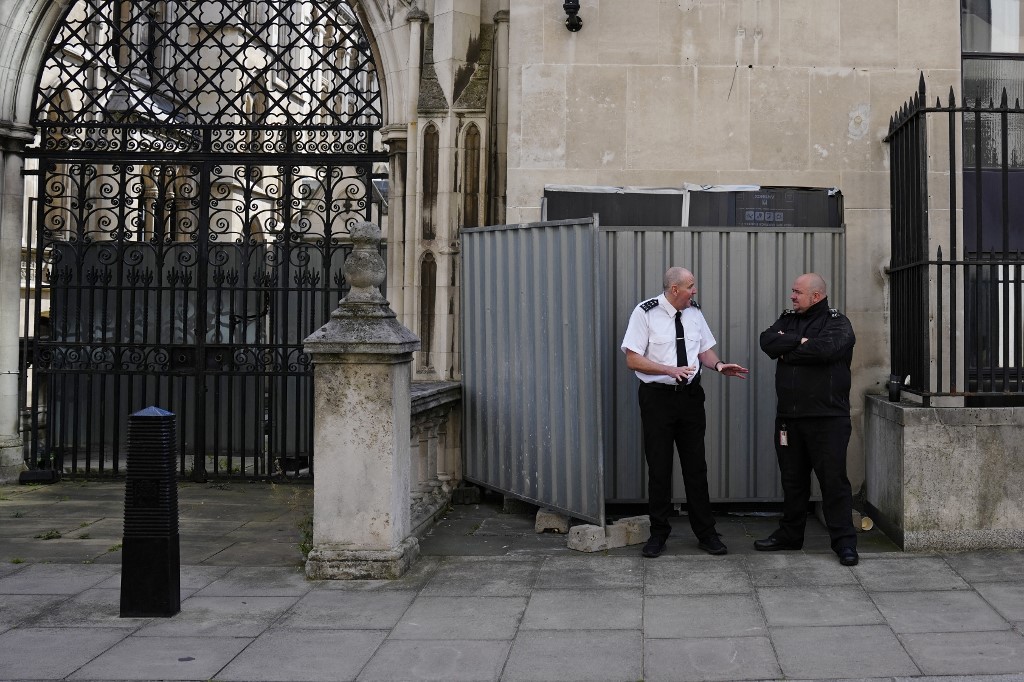Security guards stand beside a metal barrier covering up an artwork by street artist Banksy, depicting a judge using a gavel to beat a protester using a placard as protection, on an exterior wall of the Royal Courts of Justice in London, on September 8, 2025. [Carlos Jasso/AFP]