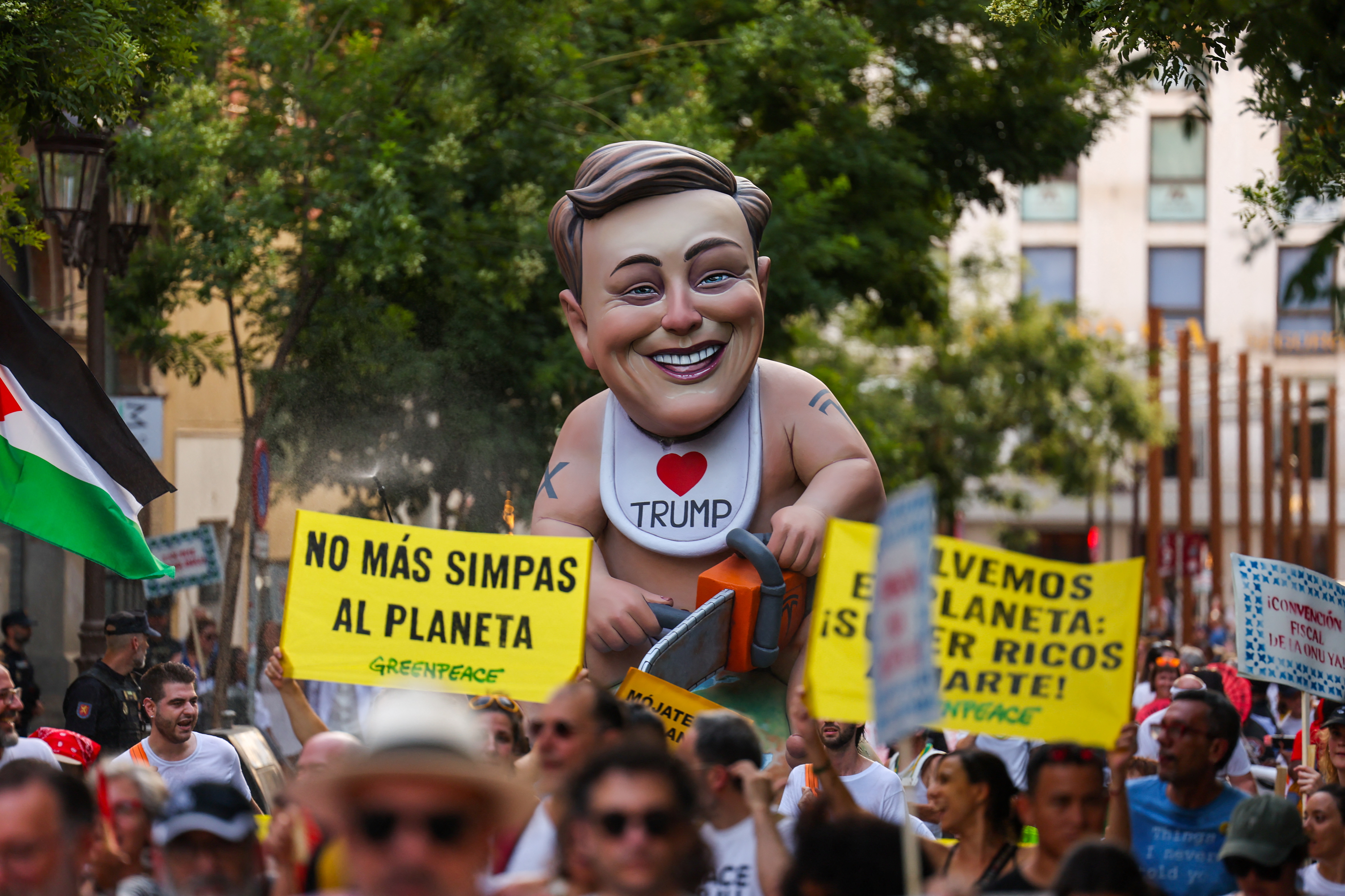 Protests in Spain show Elon Musk as a baby with an "I Heart Trump" bib.