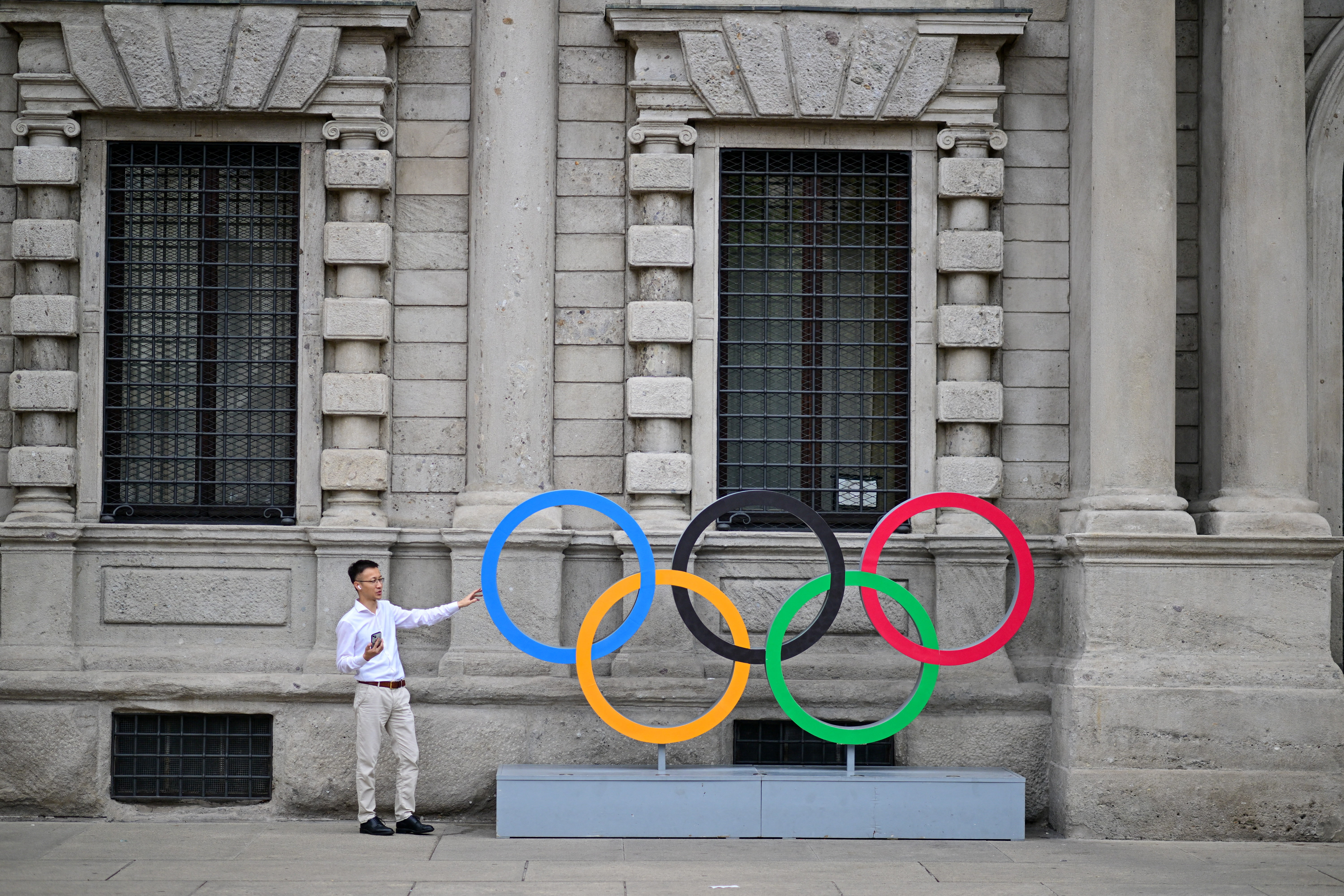 A man poses for a photograph in front of an installation depicting the Olympic Rings, on the day marking six months until the start of the Winter Olympics in Milan, Italy, August 6