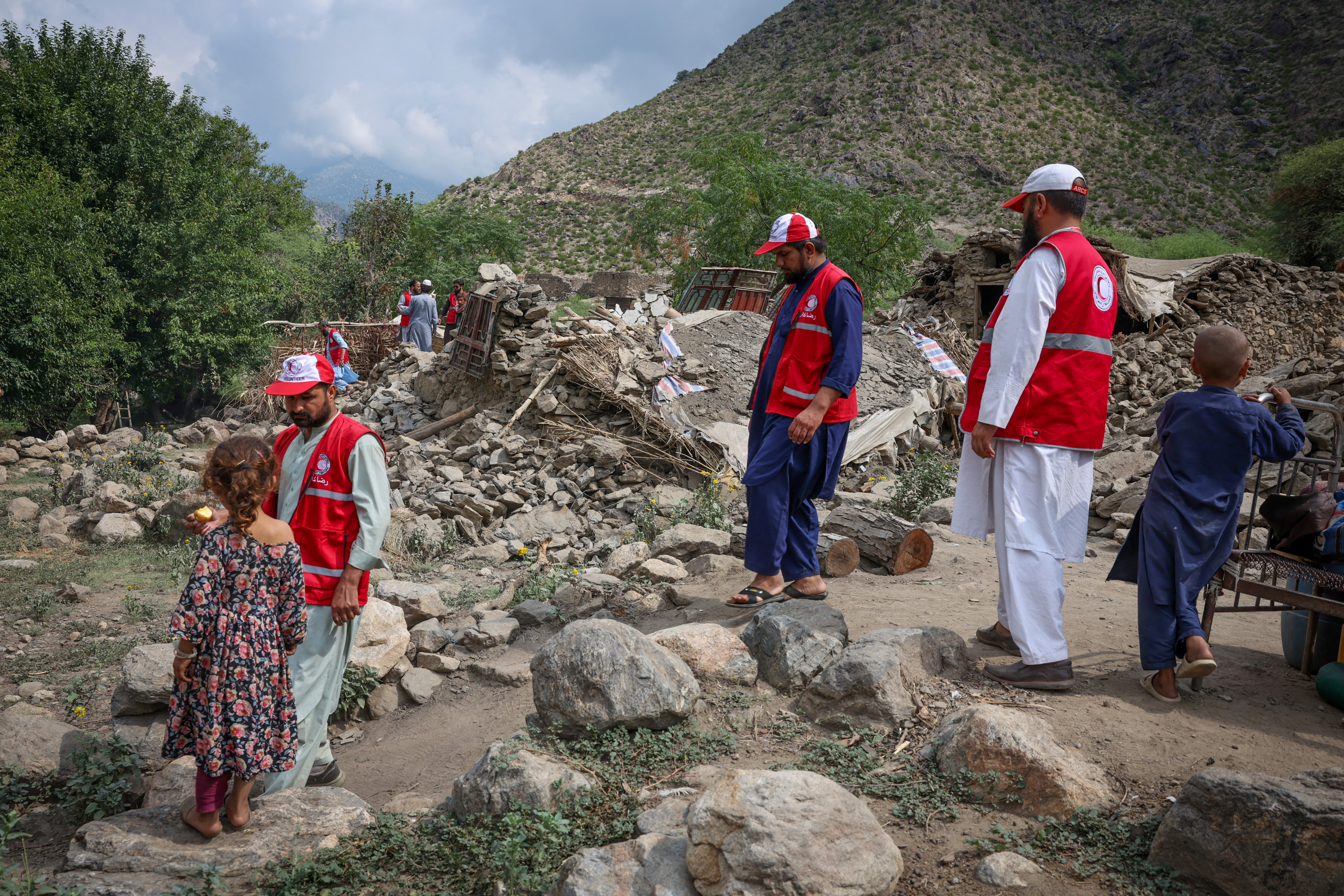 Red Crescent volunteers walk next to damaged houses following a deadly magnitude-6 earthquake that struck Afghanistan [Sayed Hassib/REUTERS]