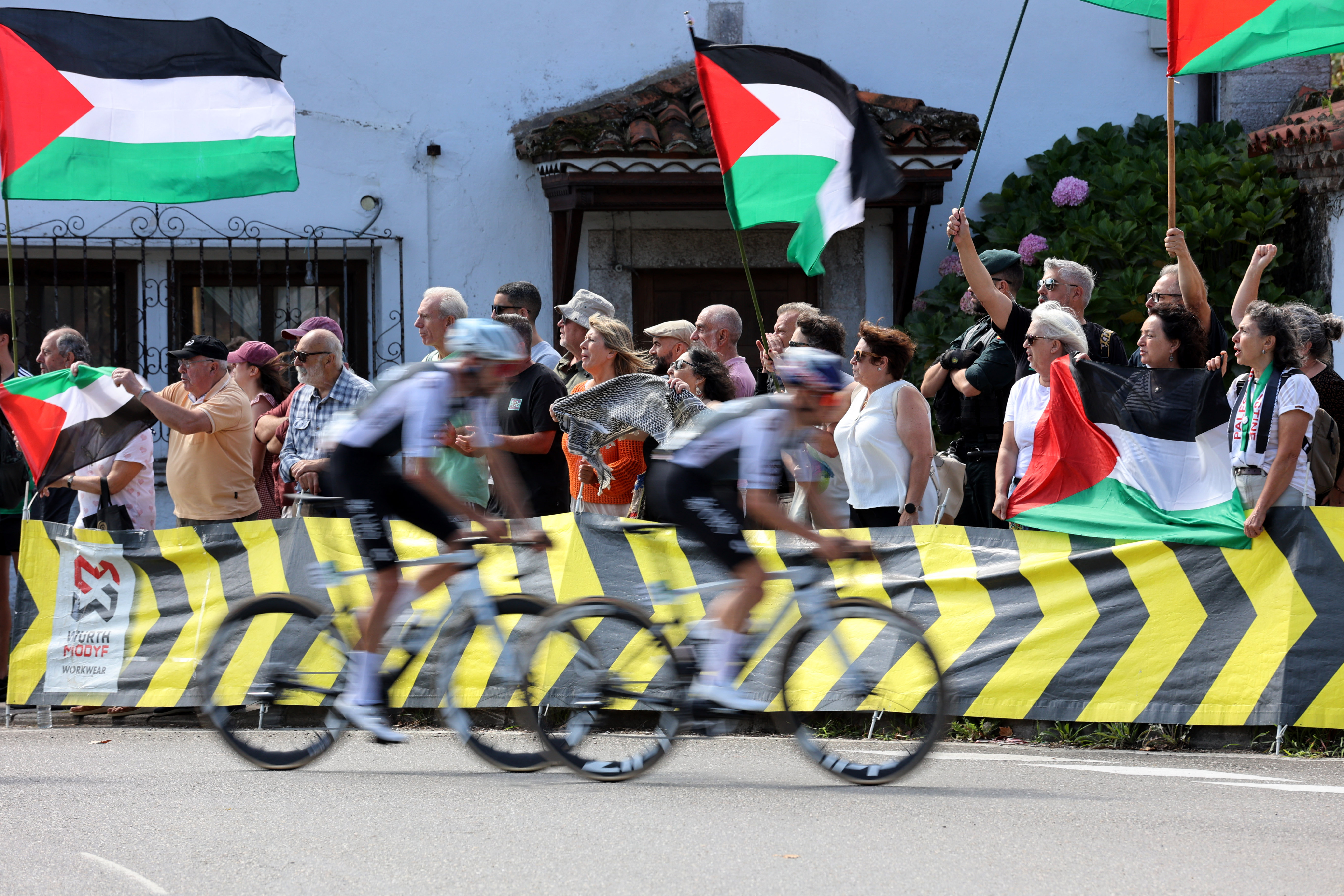 Cycling - Vuelta a Espana - Cabezon de la Sal to L'angliru - Cantabria, Spain - Riders pass protesters with Palestine flags during stage 13